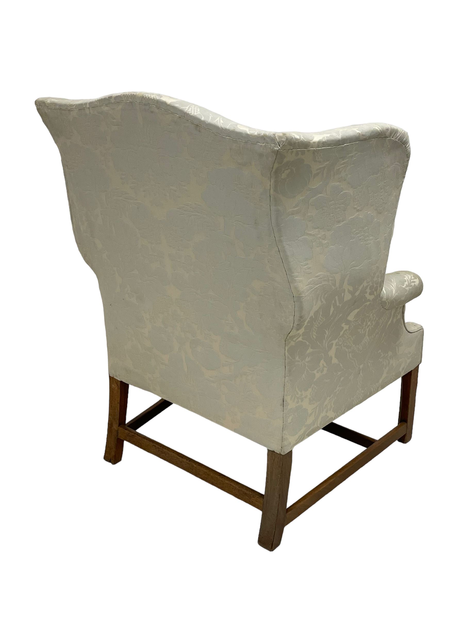 Georgian mahogany framed wingback armchair, upholstered in floral pattern silk damask fabric, wide seat enclosed by rolled arms, on chamfered square supports united by plain stretchers 