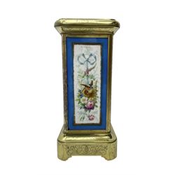 French - late 19th century 8-day mantle clock in an engraved brass corniche case with three rectangular porcelain panels decorated in the romantic Sevres style, dial with brass hands, cartouche Roman numerals and a depiction of cupid to the dial centre, rack striking movement sounding the hours and half hours on a bell. With pendulum.