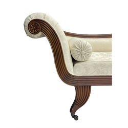 Regency design mahogany chaise longue, scrolled arms with carved rosette details, upholstered in cream damask fabric with bolster cushion, reeded frame supported by turned legs on brass castors