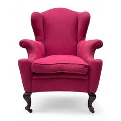 Georgian design hardwood-framed wingback armchair, arched cresting rail over curved wingback, rolled arms on scrolled cushioned supports, reverse bow-front, upholstered in claret red fabric with loose seat cushion, on cabriole front feet and brass castors 