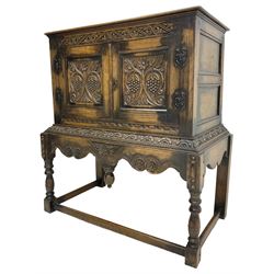 Jacobean Revival carved oak cupboard, moulded rectangular top over S-scroll carved frieze and two doors, the panelled doors carved with stylised plant motifs, on stand decorated with lunettes and shaped apron with hanging turned pendant, on turned supports united by stretchers 