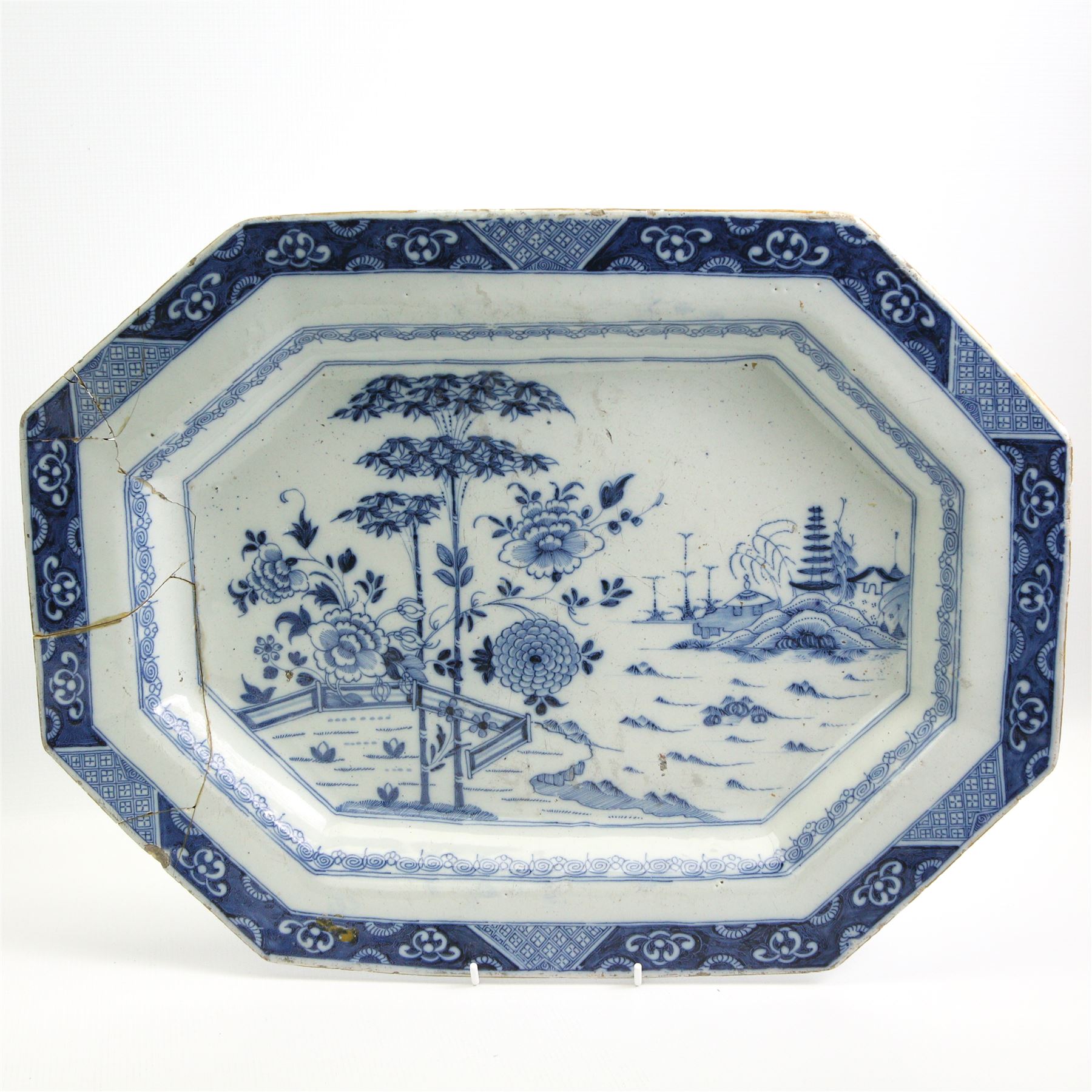 Two English Delft dishes, of canted rectangular form, painted with a fence, flowering plants and bamboo, within a scroll border, one marked F beneath, 49.5cm x 37.5cm max (2)