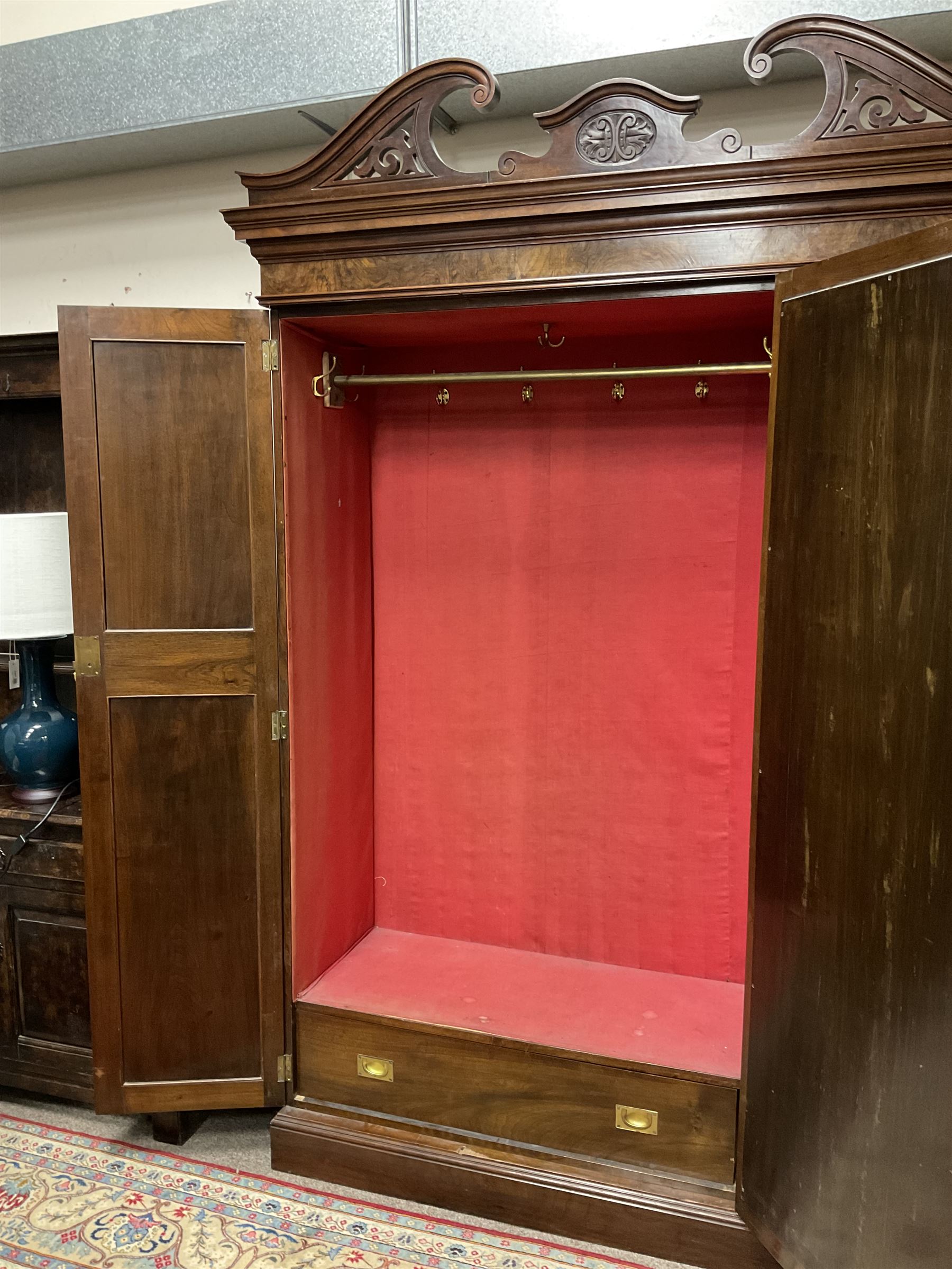 Late Victorian walnut triple wardrobe, the pierced broken swan neck pediment carved with foliate C-scrolls, central bevelled mirror door flanked by two panelled doors, the panels carved with urns, C-scrolls and trailing foliage, the interior fitted with hanging rails, long and short drawer, on moulded plinth base