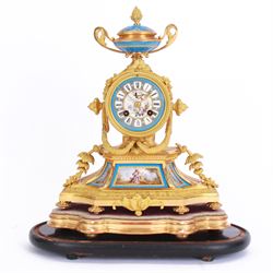 French - 19th century Sevres style porcelain inset 8-day mantle clock with an over out swept base and foliate scrolls,  porcelain panels painted with romantic scenes within gilt highlighted blue borders, dial surmounted by a conforming oval porcelain urn with side handles, blue porcelain dial with a painted centre and contrasting white cartouche Roman numerals and gilt spade hands, dial inscribed Thomas Kirk, Paris, with a rack striking twin train movement, striking the hours and half hours on a bell, mounted on a gesso padded base and ebonised plinth. With key and pendulum.