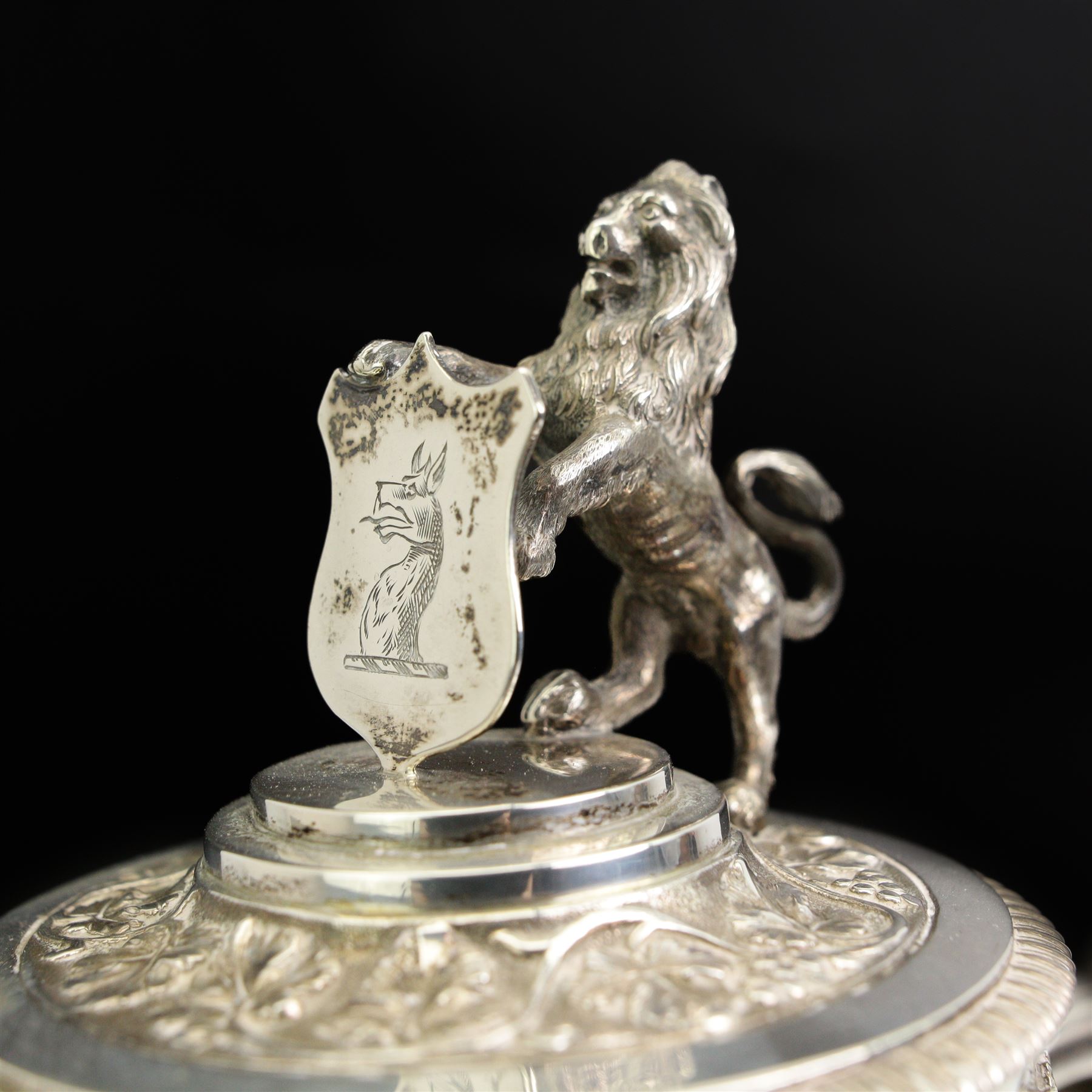 Victorian silver-mounted glass claret jug by George Richards Elkington, with Bacchanalian repoussé decoration and mask spout, with a domed hinged cover with a thumb-piece modelled as a rampant lion holding a shield, with engraved Dragon head crest, the glass body with etched greek key border and star-cut base, H29cm 