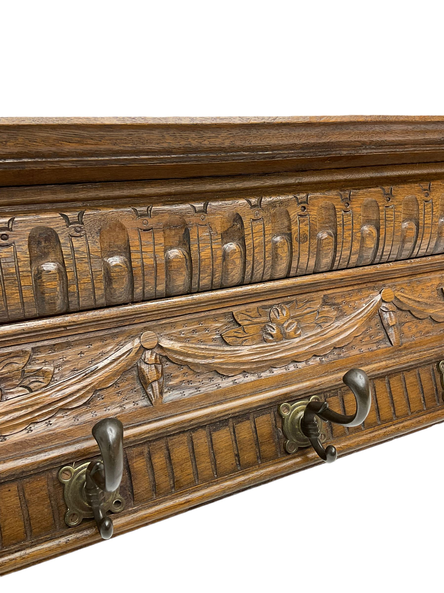 Late 20th century carved oak wall hanging coat rack, projecting moulded lintel over arcade carved frieze, flanked by two carved masks, fitted with five foliate cast hooks