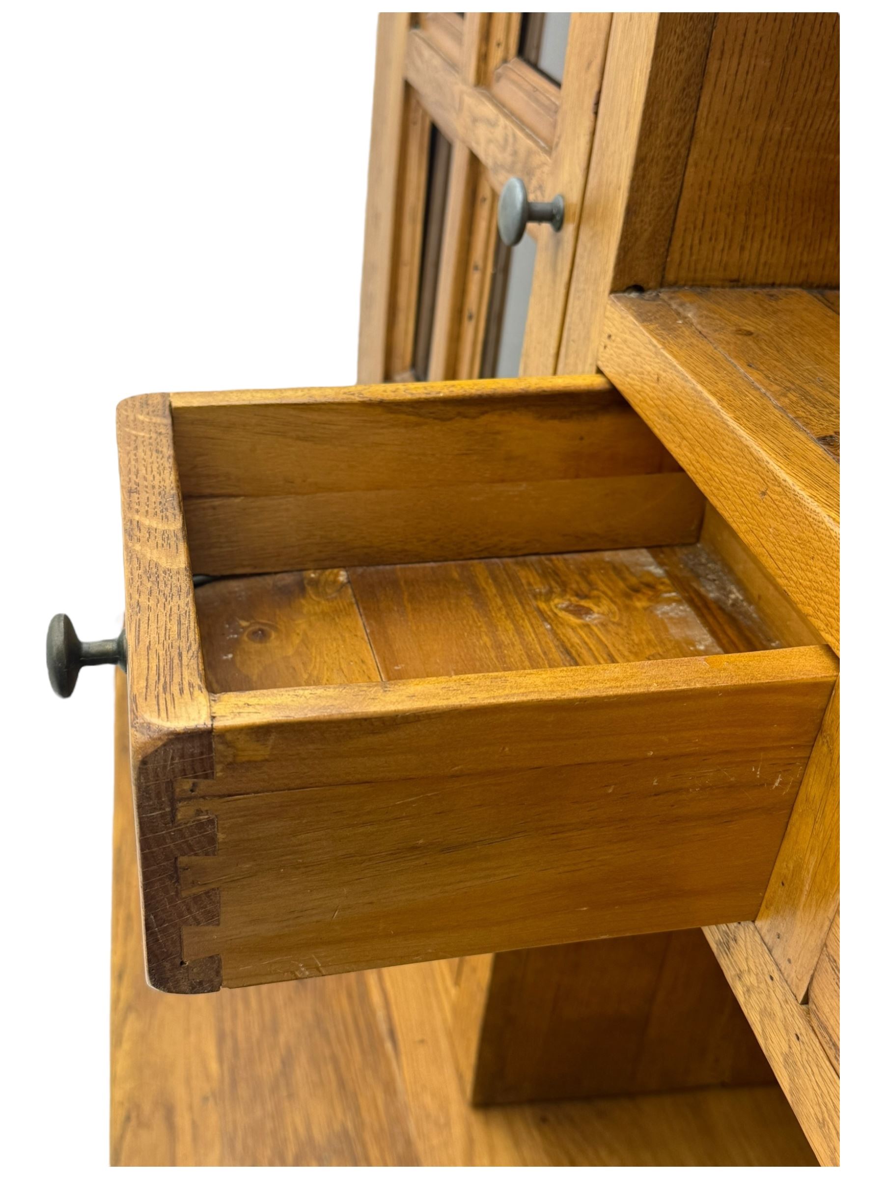 Oak dresser, upper section with twin glazed cupboard doors and central shelving with two trinket drawers, lower section fitted with six drawers over three panelled cupboard doors, raised on shaped feet 