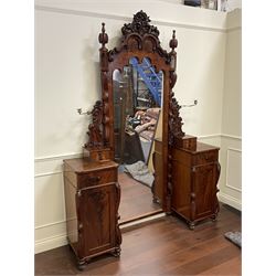 Tall Victorian figured mahogany twin pedestal dressing table, the tall mirror with flower head and scrolled leaf carved pediment, flanked by two turned and carved finials over faceted lancet arched lantern tops, plane mirror plate enclosed by shaped frame, pierced and undulating moulded uprights, on C-scroll and curled leaf carved supports fitted with cast brass hinged candle sconces, each pedestal fitted with two small trinket drawers over larger drawer and panelled cupboard, canted corners with matched upright mounts, the cupboard doors enclosing slides, on scroll carved feet 