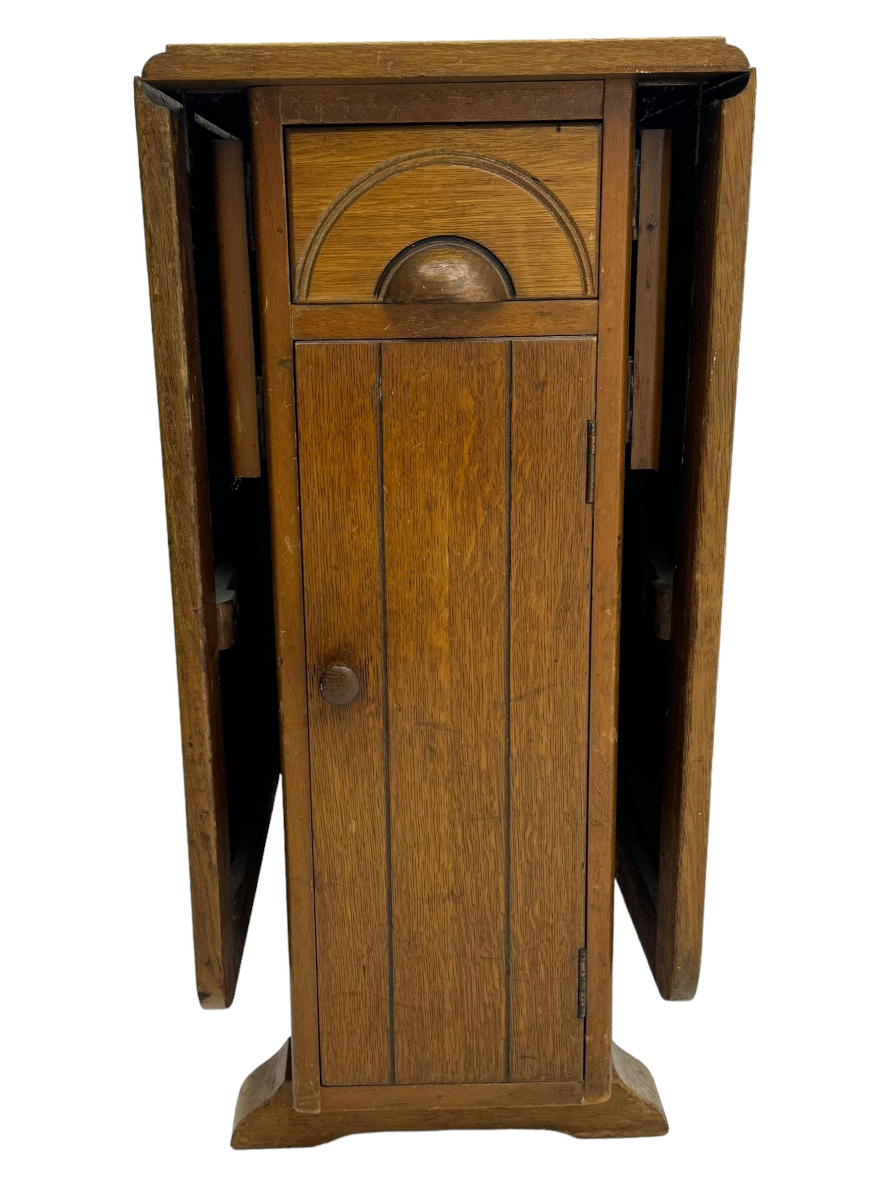 Early 20th century oak drop-leaf table, in the style of Harris Lebus, featuring rectangular top over central pedestal base, with two drawers and two cupboards, on gateleg supports