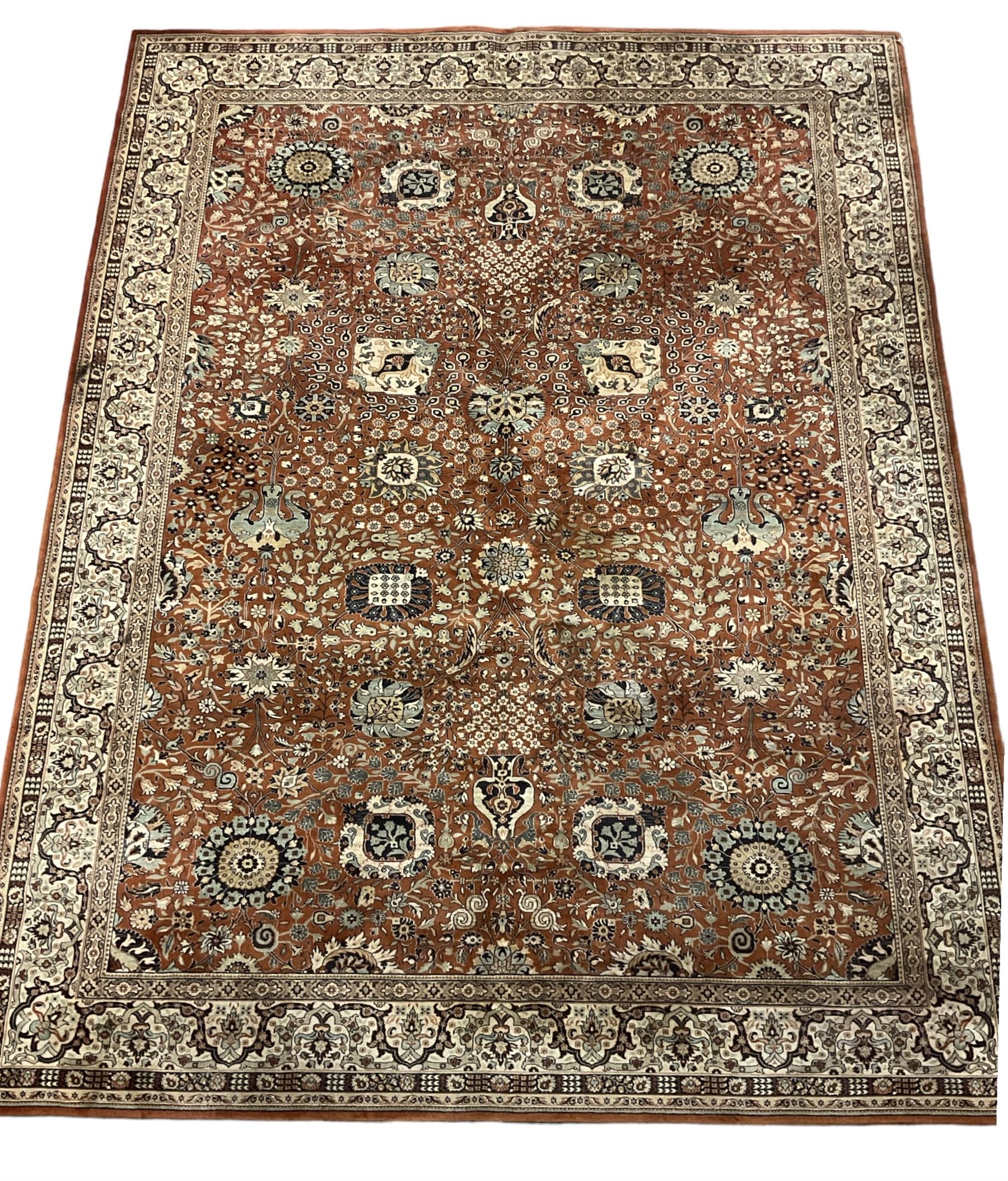 Persian design carpet, rust ground field decorated with large stylised plant motifs surrounded by smaller floral motifs, repeating trailing border