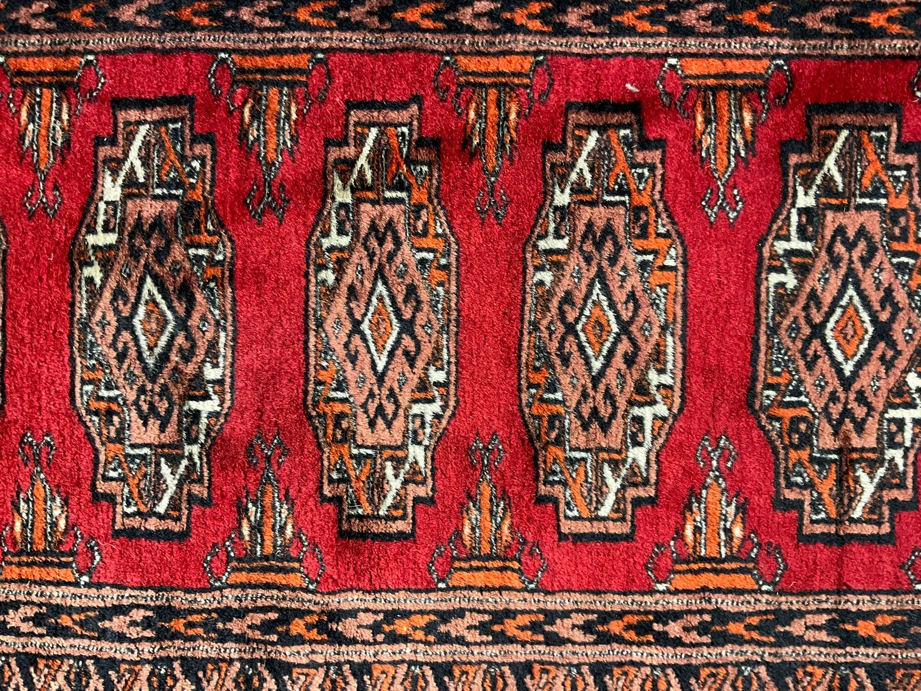 Persian Bokhara dark amber round rug, crimson field with six Gul motifs, surrounded by a guarded border with geometric design (124cm x 70cm); together with another similar in amber and red (101cm x 63cm) (2)