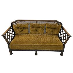 Early 20th century three-piece bergère suite - three seat sofa (W177cm, H82cm, D75cm); pair of matching armchairs (W84cm); single caned back with 'cock-pen' panelled arms, upholstered in foliate pattern fabric, blind fretwork lower frieze over square feet 