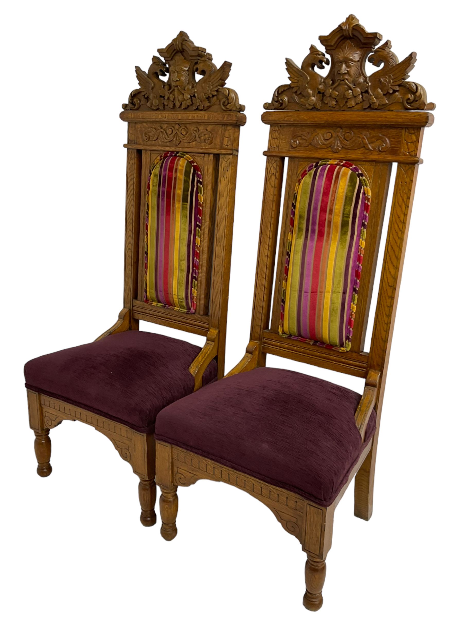 Set of six 20th century Carolean design oak high back chairs, the pediment carved with dragons and central Green Man mask with trailing foliage, the backs upholstered in striped fabric, on turned front supports