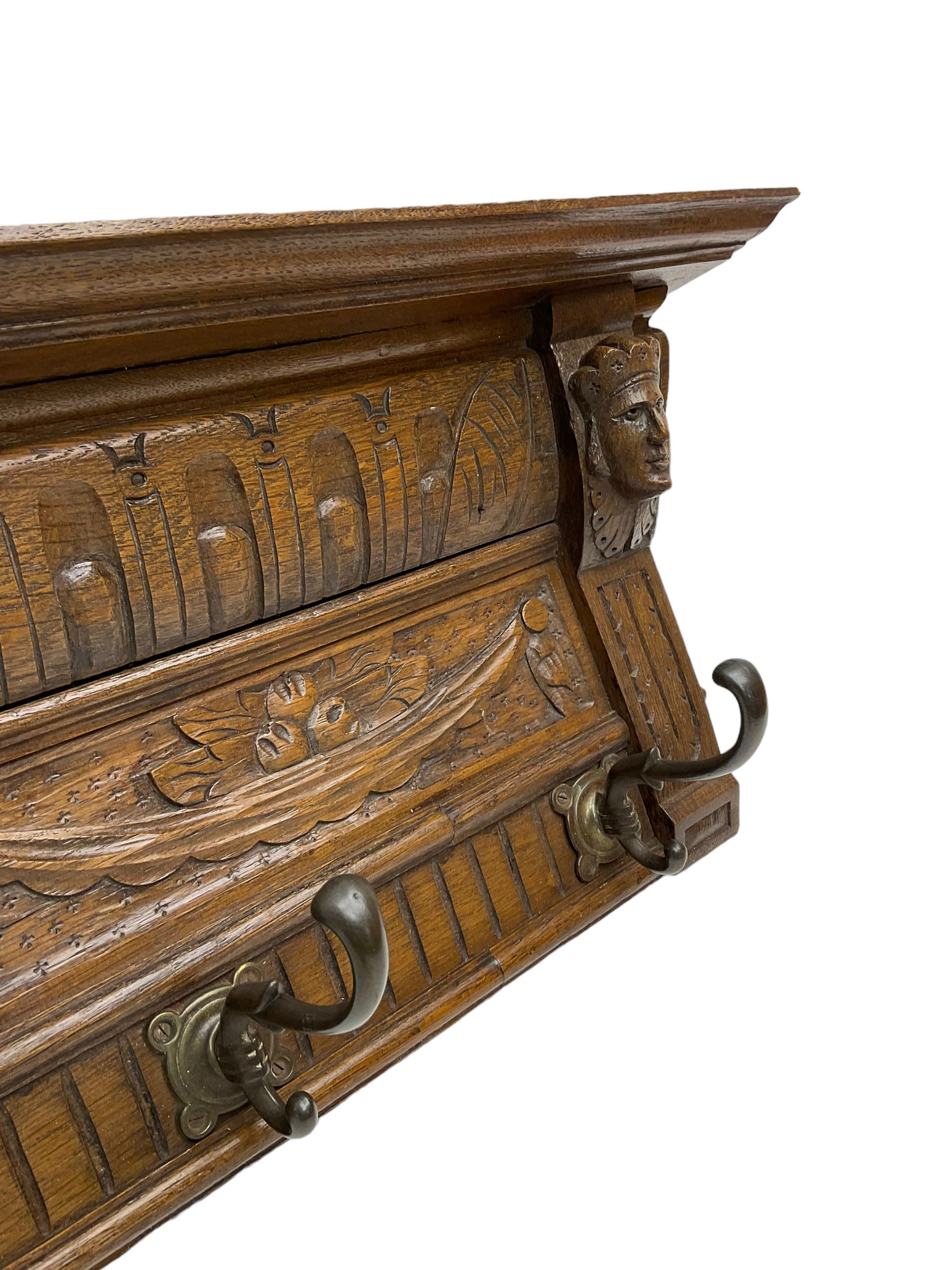 Late 20th century carved oak wall hanging coat rack, projecting moulded lintel over arcade carved frieze, flanked by two carved masks, fitted with five foliate cast hooks