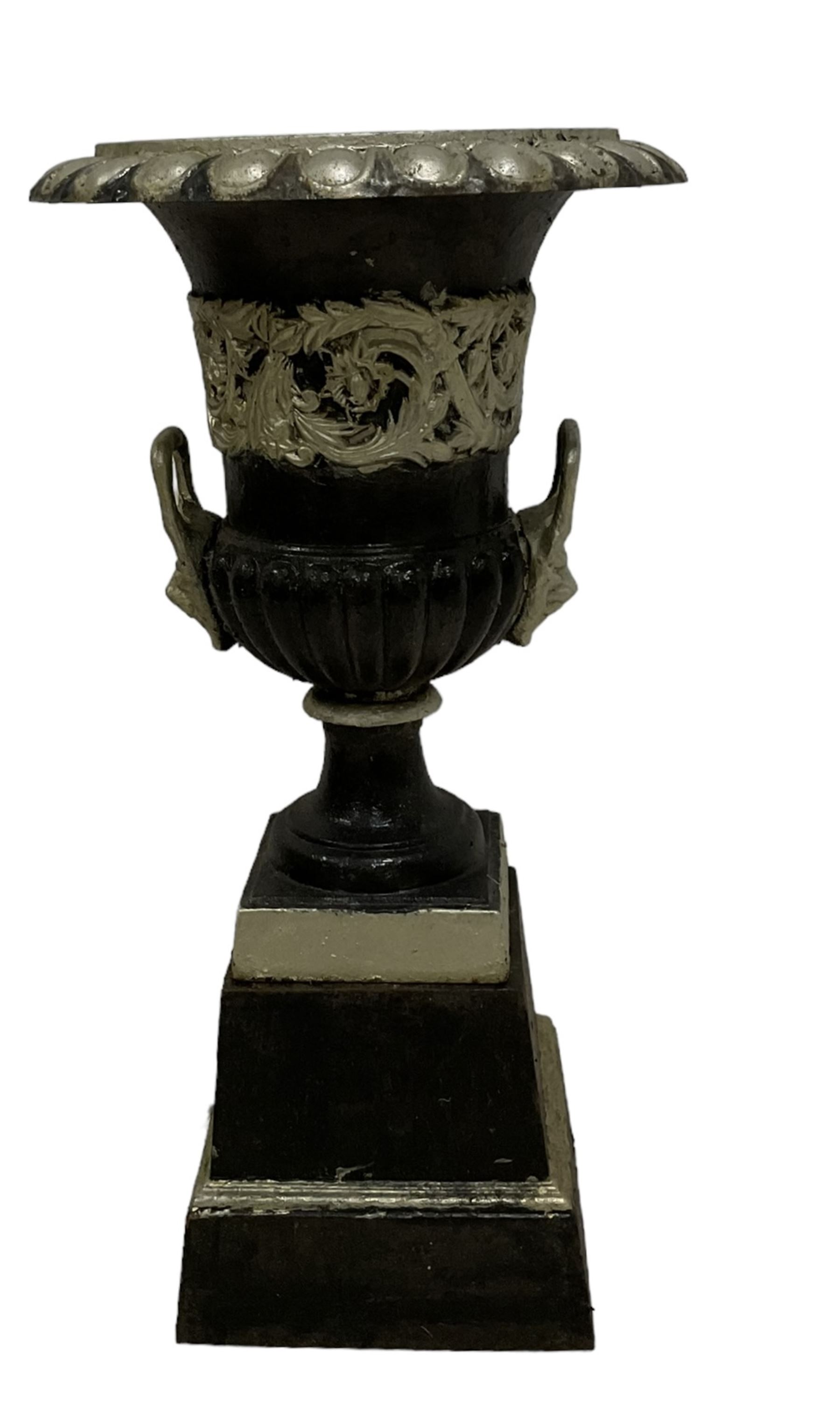 20th century cast iron Campana-shaped urn on plinth, with scrolling foliate relief decoration, in ebonised and silver painted finish