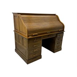 Early 20th century oak tambour roll-top desk, the top with fitted interior including drawers, pigeonholes and compartments, the twin pedestals fitted with four drawers with carved handles, supported by plinth base 