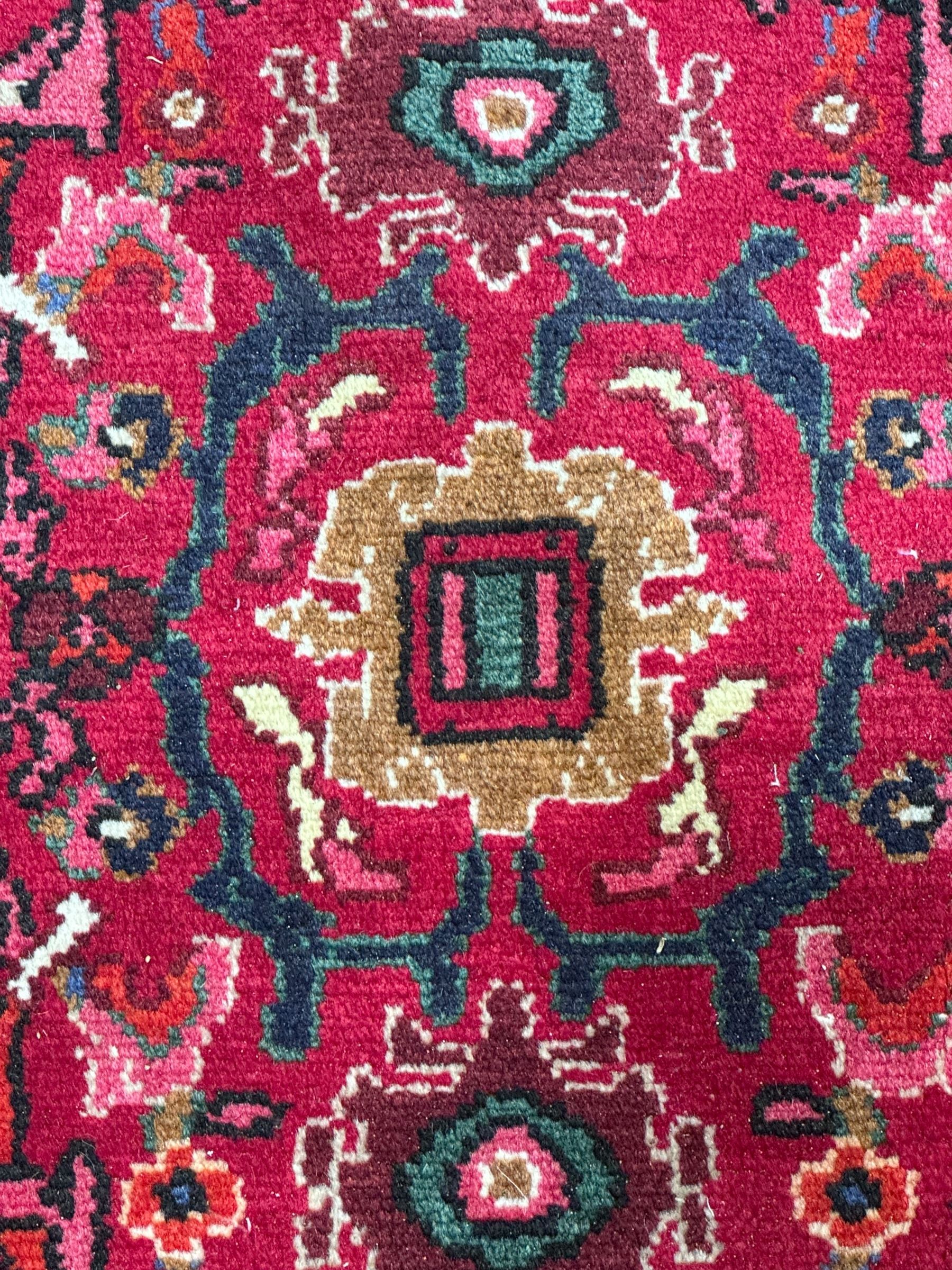 Persian Nanaj crimson ground carpet, the busy field filled with interconnecting stylised plant motifs with scrolling branches, the guarded indigo border decorated with repeating palmettes and foliate patterns