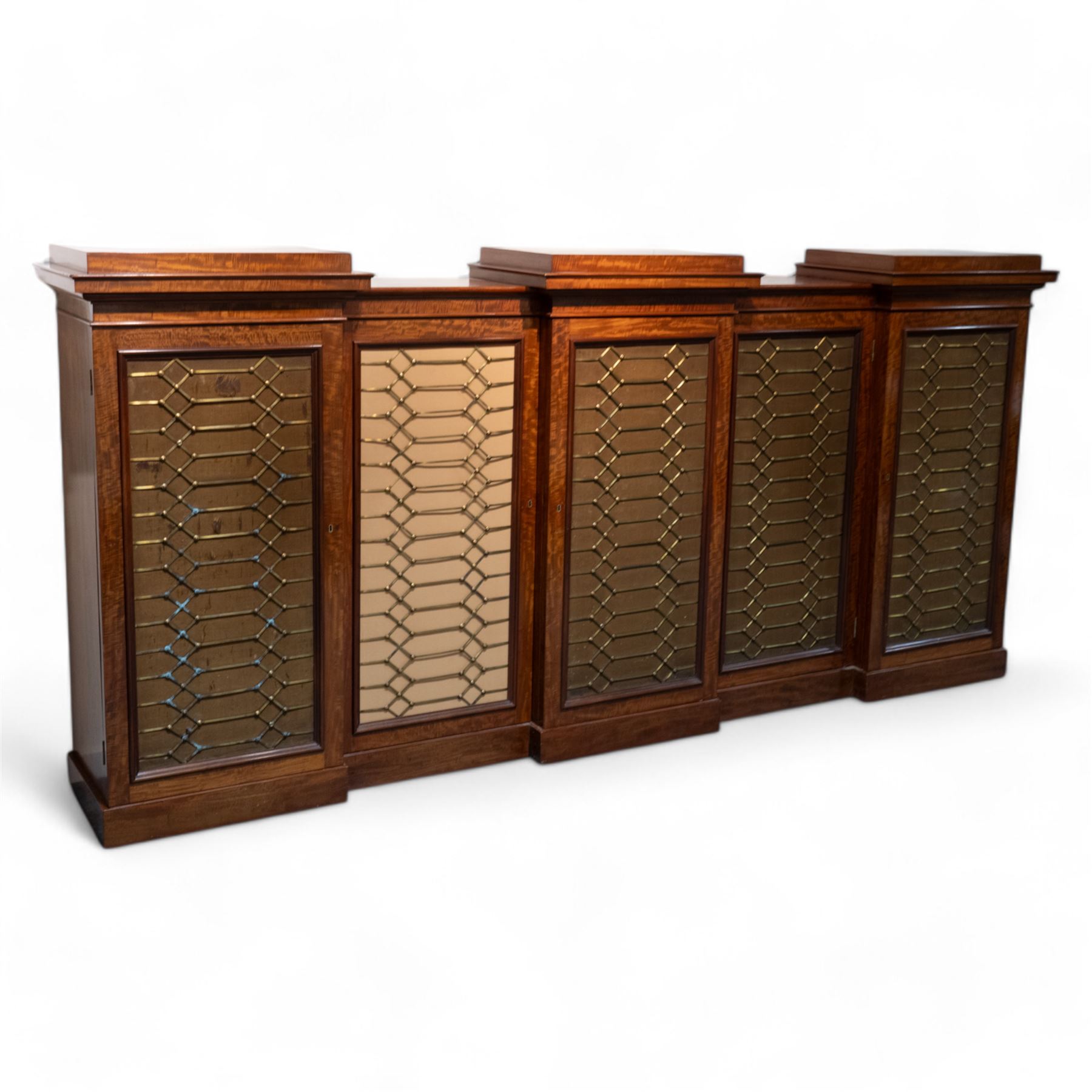 Large 19th century figured mahogany bookcase, enclosed by five brass grille panel doors, the interior fitted with adjustable shelves, double drop centre and break front with raised stepped tops, on plinth base 