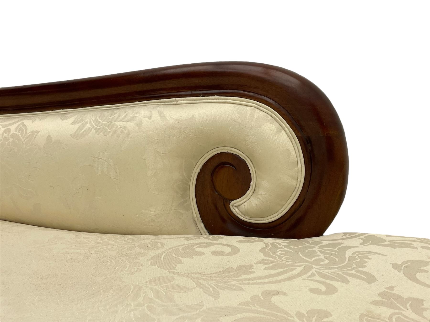 Regency design mahogany chaise longue, scrolled arms with carved rosette details, upholstered in cream damask fabric with bolster cushion, reeded frame supported by turned legs on brass castors