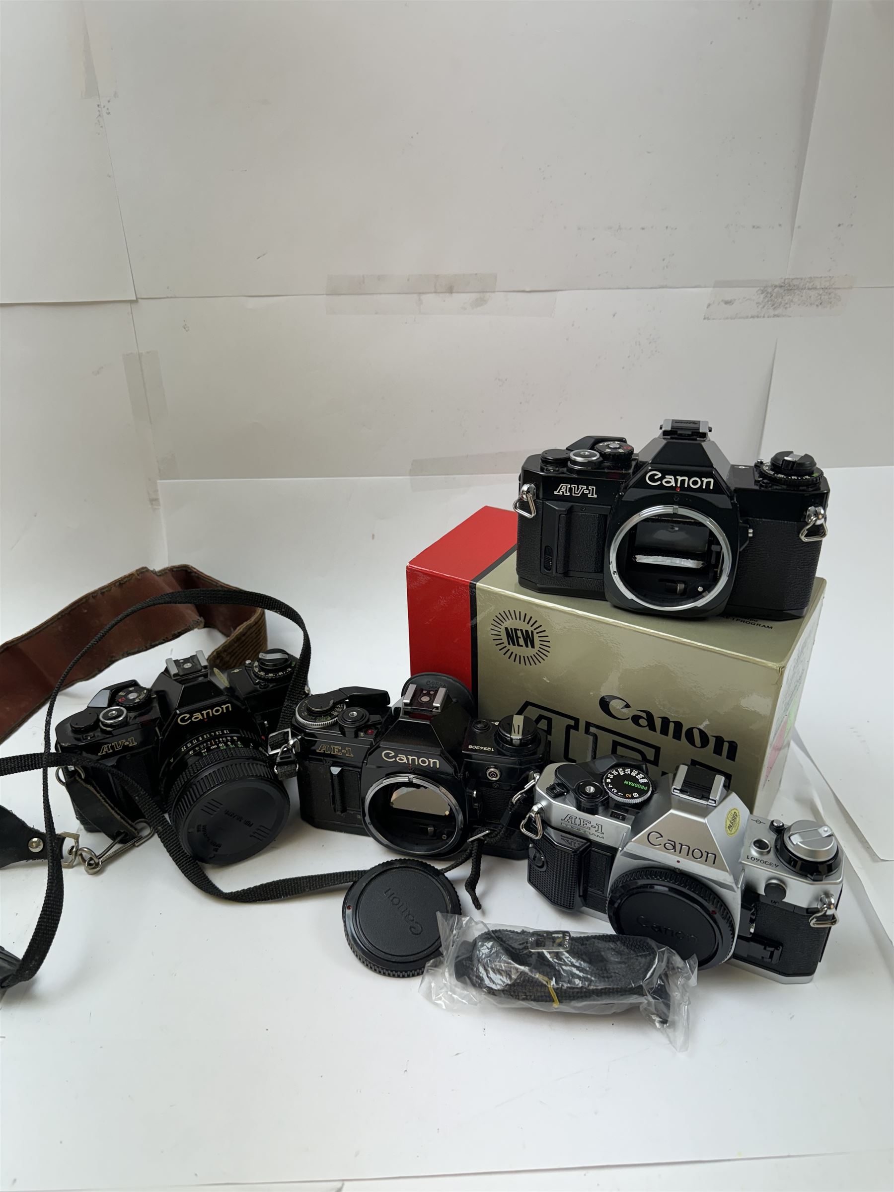 Four Canon SLR camera bodies, to include AE-1 Program, in black and silver finish, serial no. 4330401, boxed, AE-1 serial no. 1234206 and two AV-1 examples, serial nos. 841957 & 334882, one with a Canon FD 50mm 1:18 lens