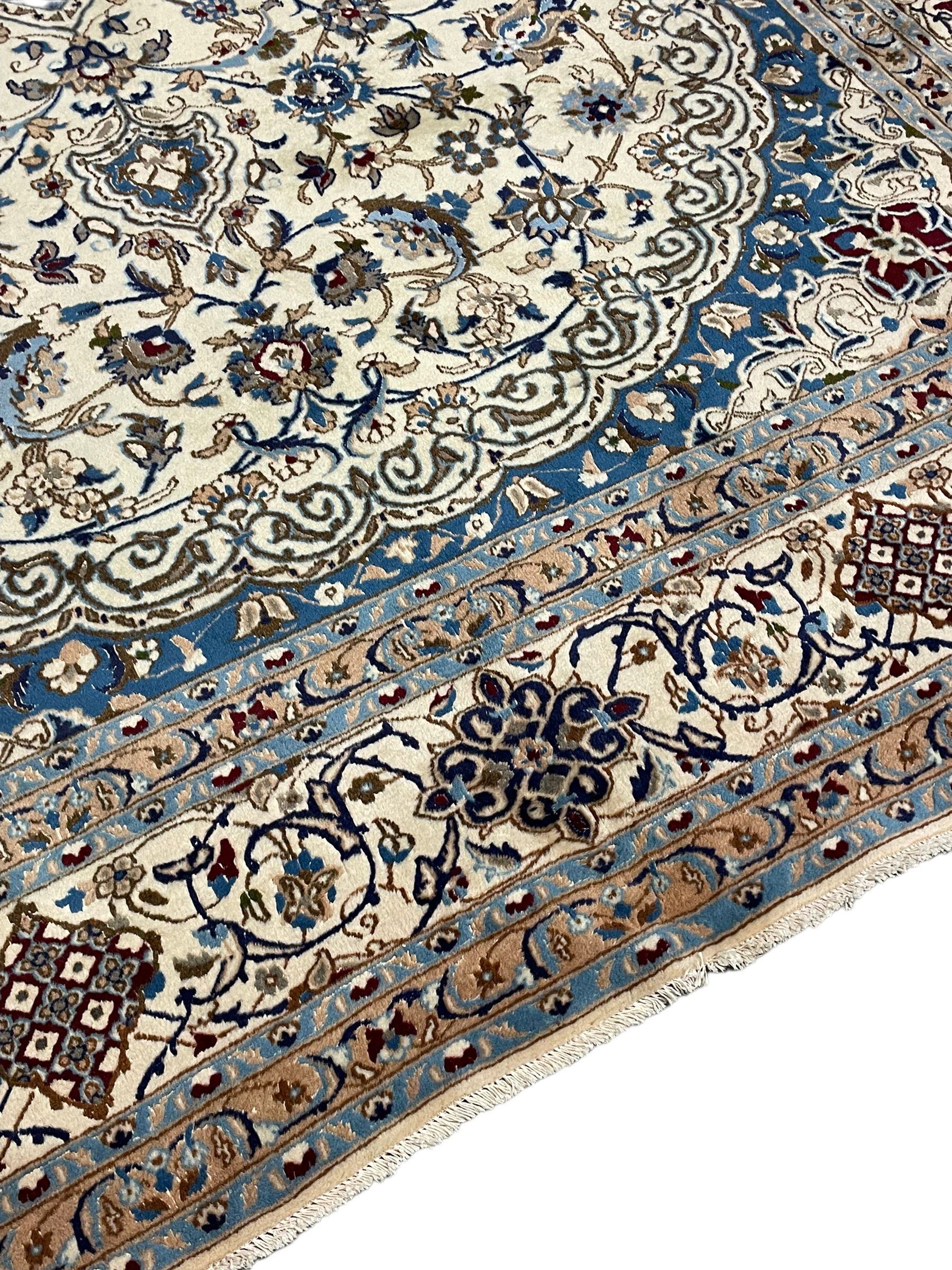 Persian Nain ivory ground carpet, the field decorated all over with leafy branches and stylised flower head motifs, blue ground central medallion and matching spandrels decorated with trailing foliate pattern, repeating guarded border with overall floral design