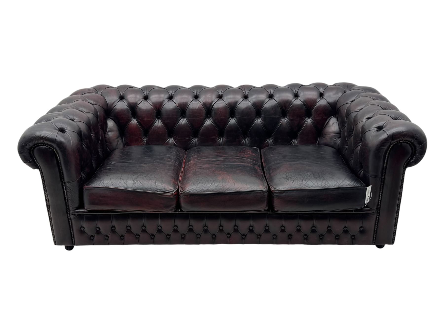 Chesterfield three-seat sofa, traditional shaped upholstered in deeply buttoned dark red leather; together with similar footstool 