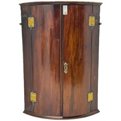 George III mahogany bow-front corner cupboard, enclosed by two figured doors with brass hinges and escutcheon, the painted interior fitted with three shelves 