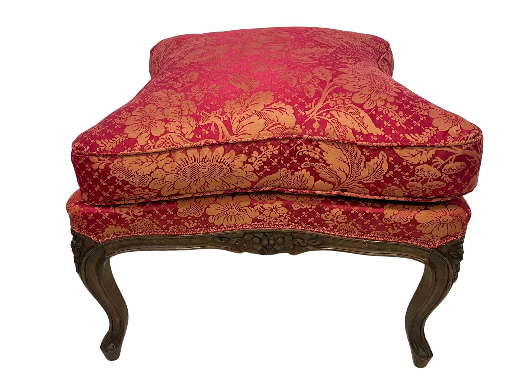 Late 20th century French design stained beech framed armchair and matching stool - the armchair with shaped and moulded frame carved with flower heads and foliage, upholstered in silk red and gold ground fabric with floral pattern, on scroll carved cabriole feet decorated with flower head carvings (W73cm, H82cm, D75cm); the footstool of concaved rectangular form with moulded frame carved with flower heads, upholstered loose cushion, on cabriole feet (70cm x 64cm, H48cm)