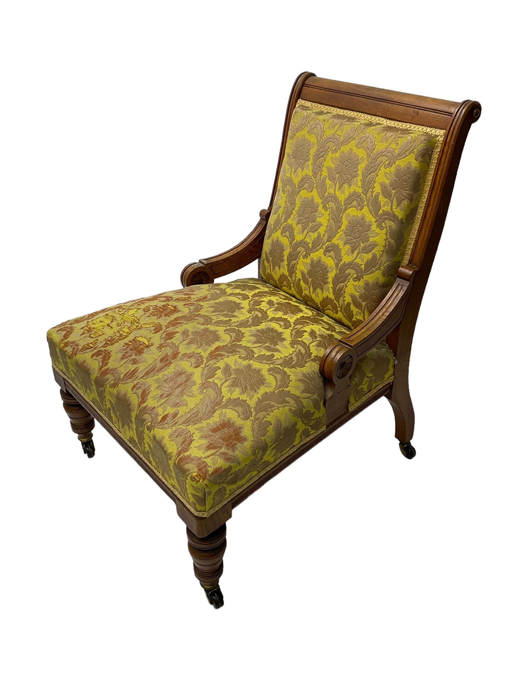 Late Victorian oak nursing chair, moulded frame with flower head carved roundels, upholstered in floral pattern fabric, on turned front feet with brass and ceramic castors 