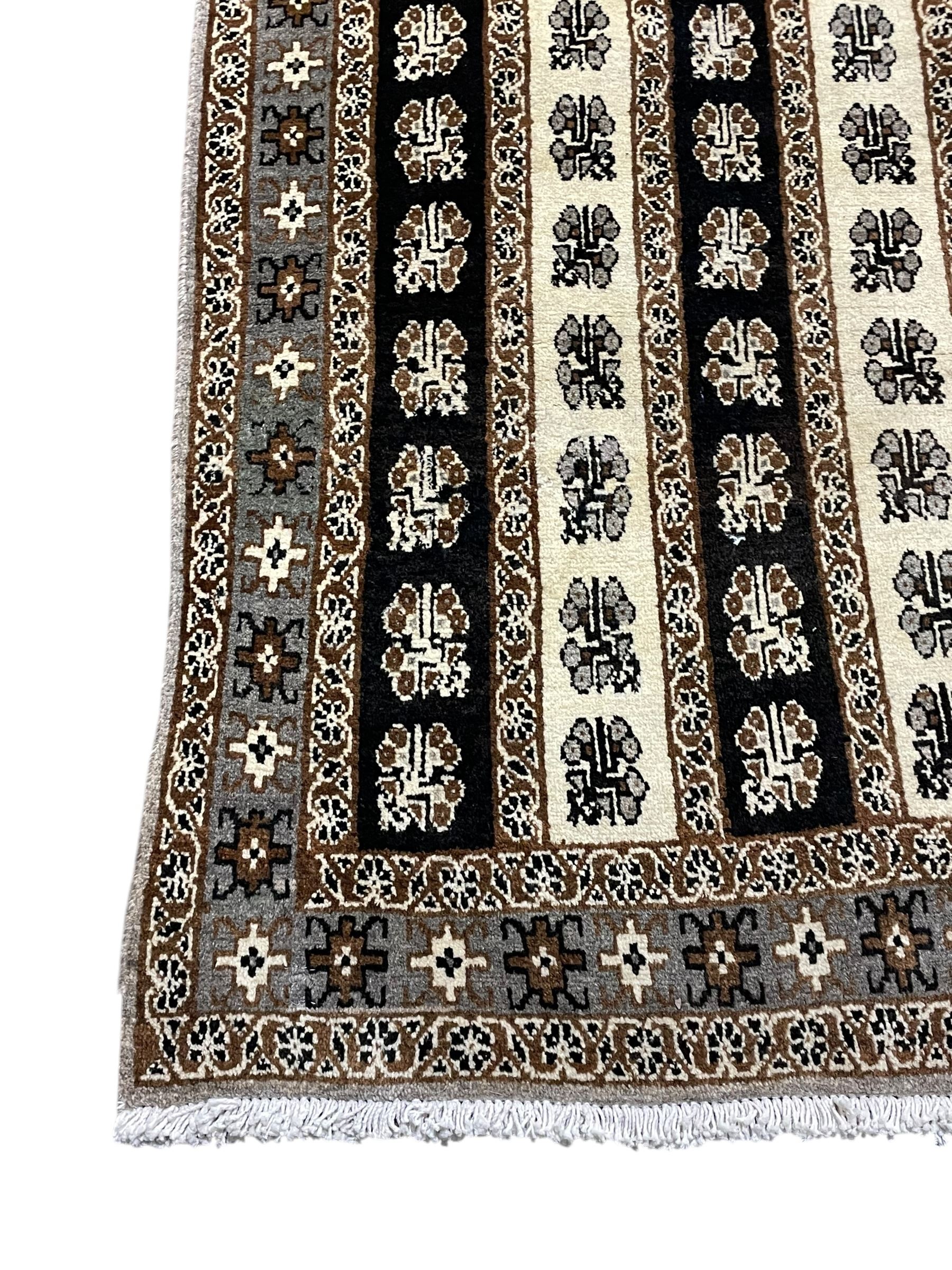 Persian ivory ground rug, the field divided into stripes decorated with stylised flower heads, the border with repeating cross motifs within guard stripes 