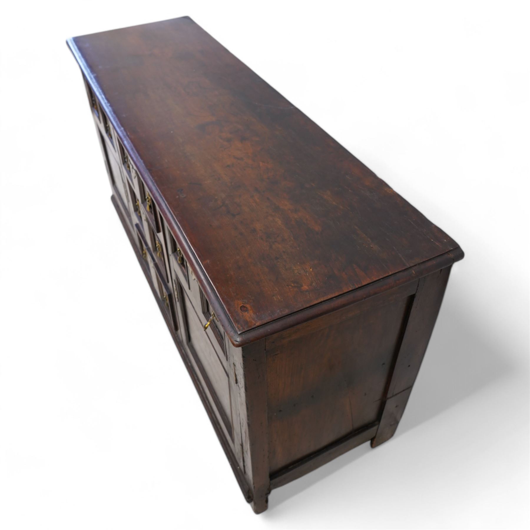 George III elm dresser base, the rectangular top with moulded edge, fitted with three central graduating twin-panelled drawers, flanked by two cupboard doors moulded with false drawer facias over large panels, lower moulded edge over stile feet