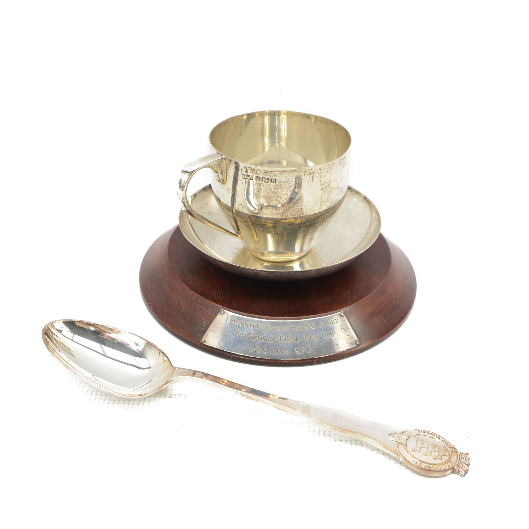 Silver trophy in the form of a cup and saucer 'Brooke Bond Tea Cup, Ayr, May 1976 presented to the winning owner' on wooden plinth Sheffield 1976 Maker Mappin & Webb and a silver spoon inscribed 'Goodwood Racecourse' L24cm (2) 