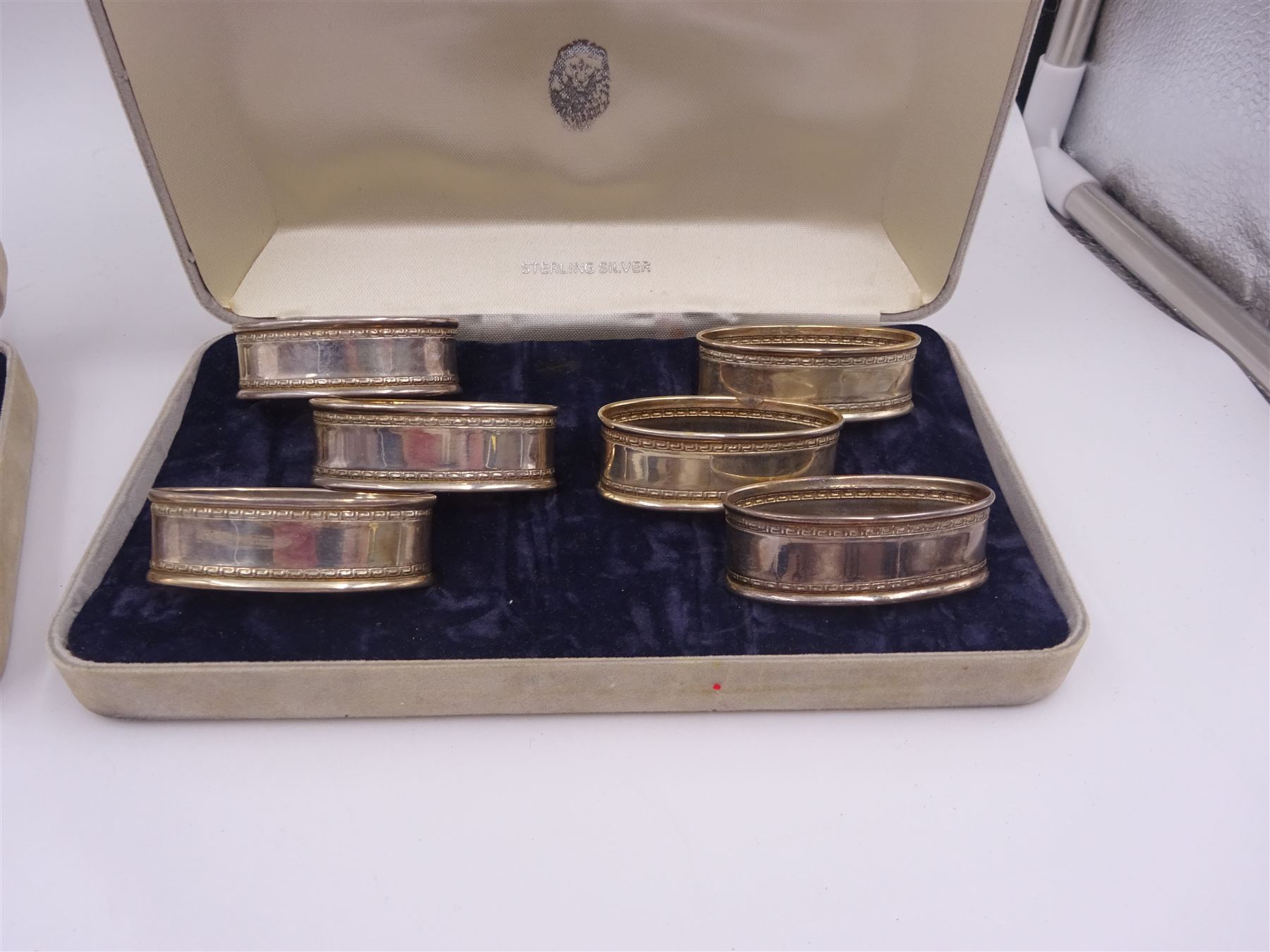 Two sets of six modern silver napkin rings, each of oval form, with Greek key decoration, hallmarked Ari D Norman, London 1986, both in fitted cases