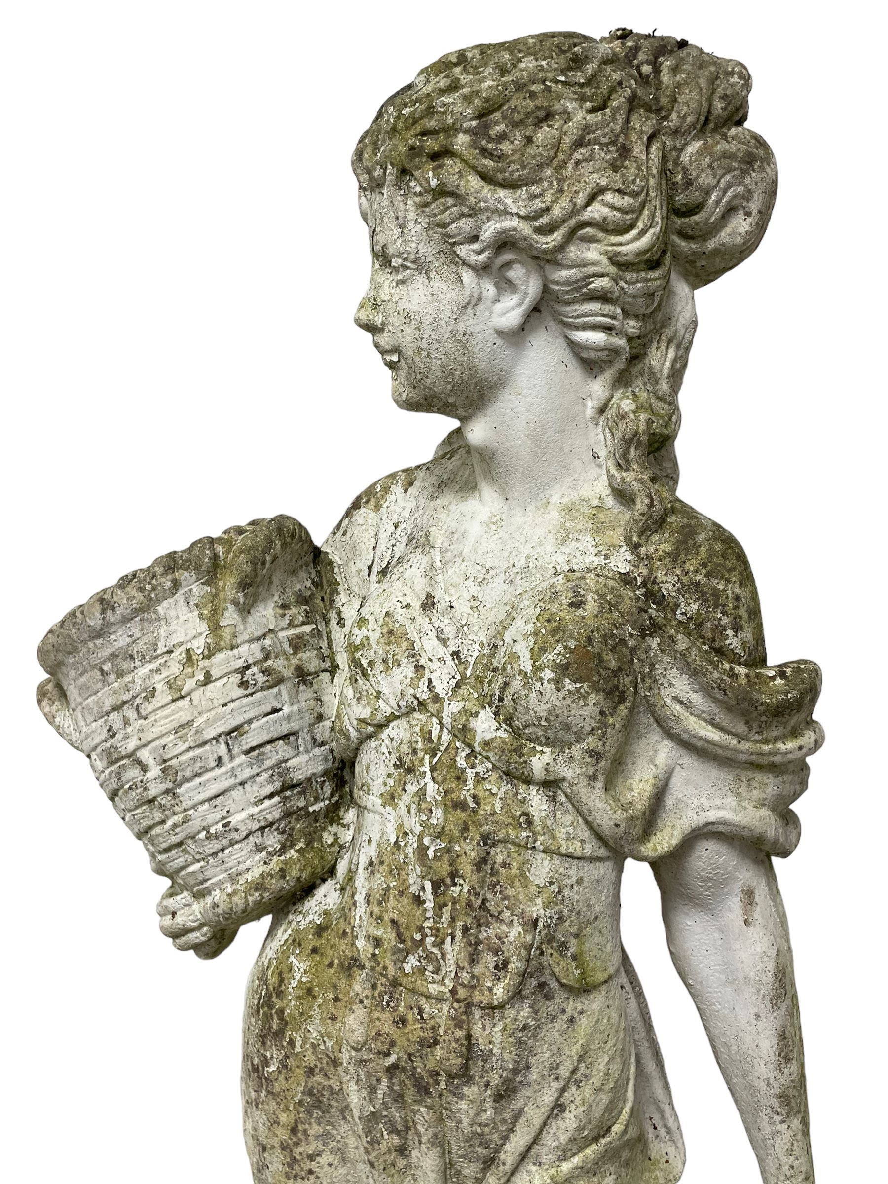 Weathered and painted cast stone garden statue, in the form of an Italian maiden carrying baskets with gathered flora and berries, on a shaped ovoid base