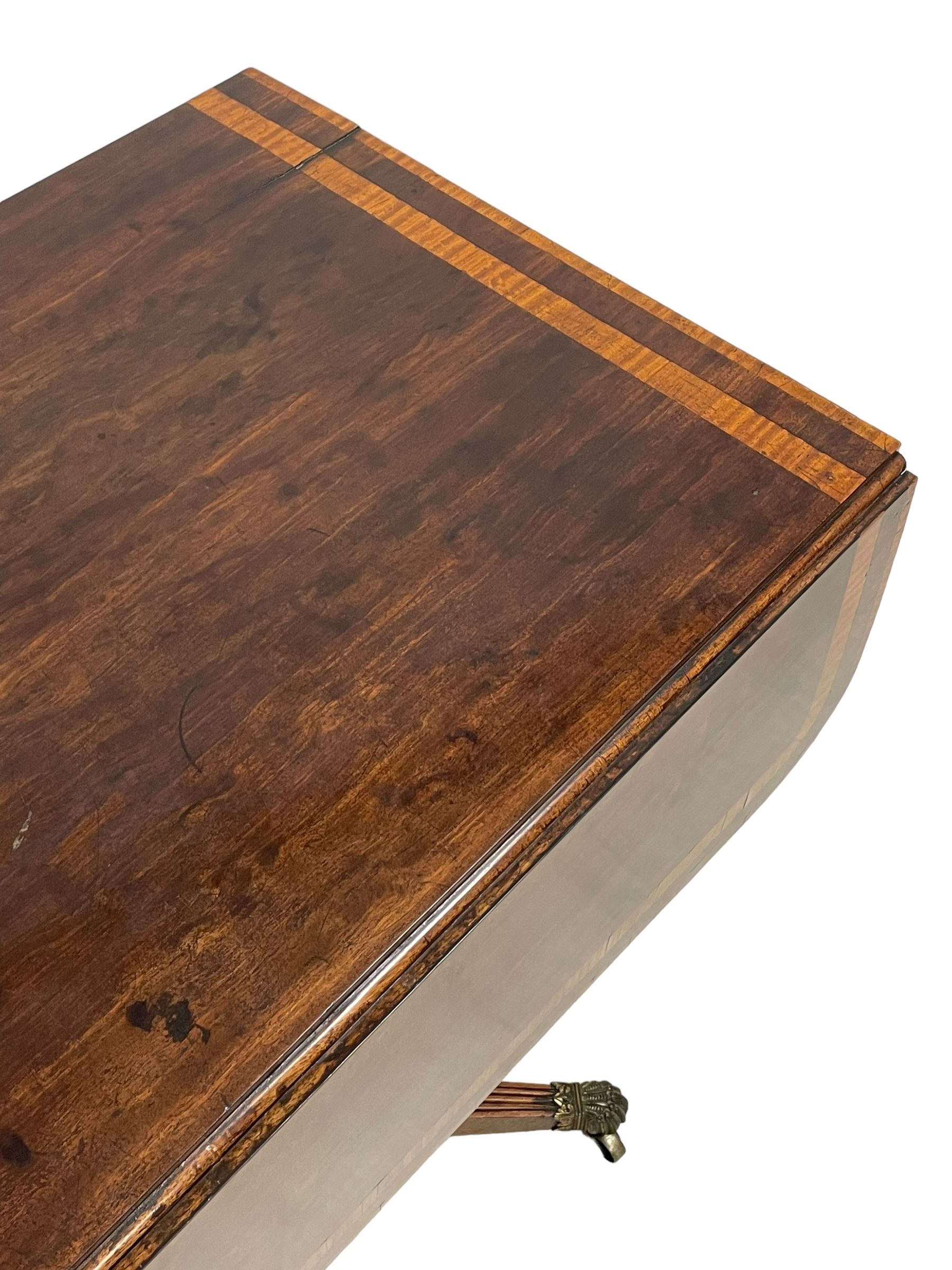 Early 19th century mahogany Pembroke table, rectangular drop-leaf top with rounded corners inlaid satinwood bands, single end drawer and opposing false drawer, turned pedestal on four acanthus carved and reed moulded splayed supports, cast brass cups and castors 