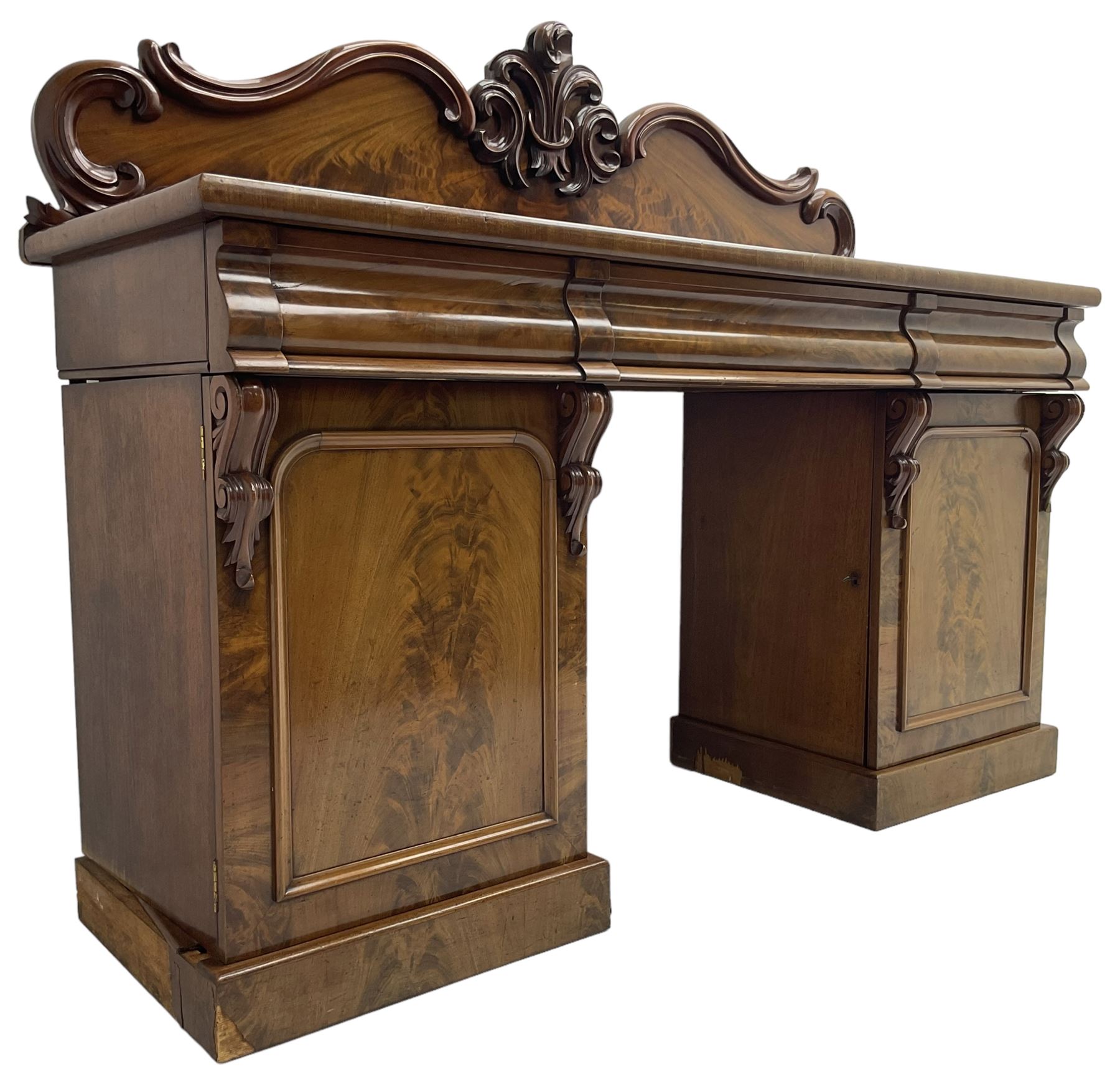 Victorian mahogany twin pedestal chiffonier, raised back with decorated with scrolling foliate motifs, fitted with three cushion drawers, the arched panelled pedestals enclosing shelves and sliding trays