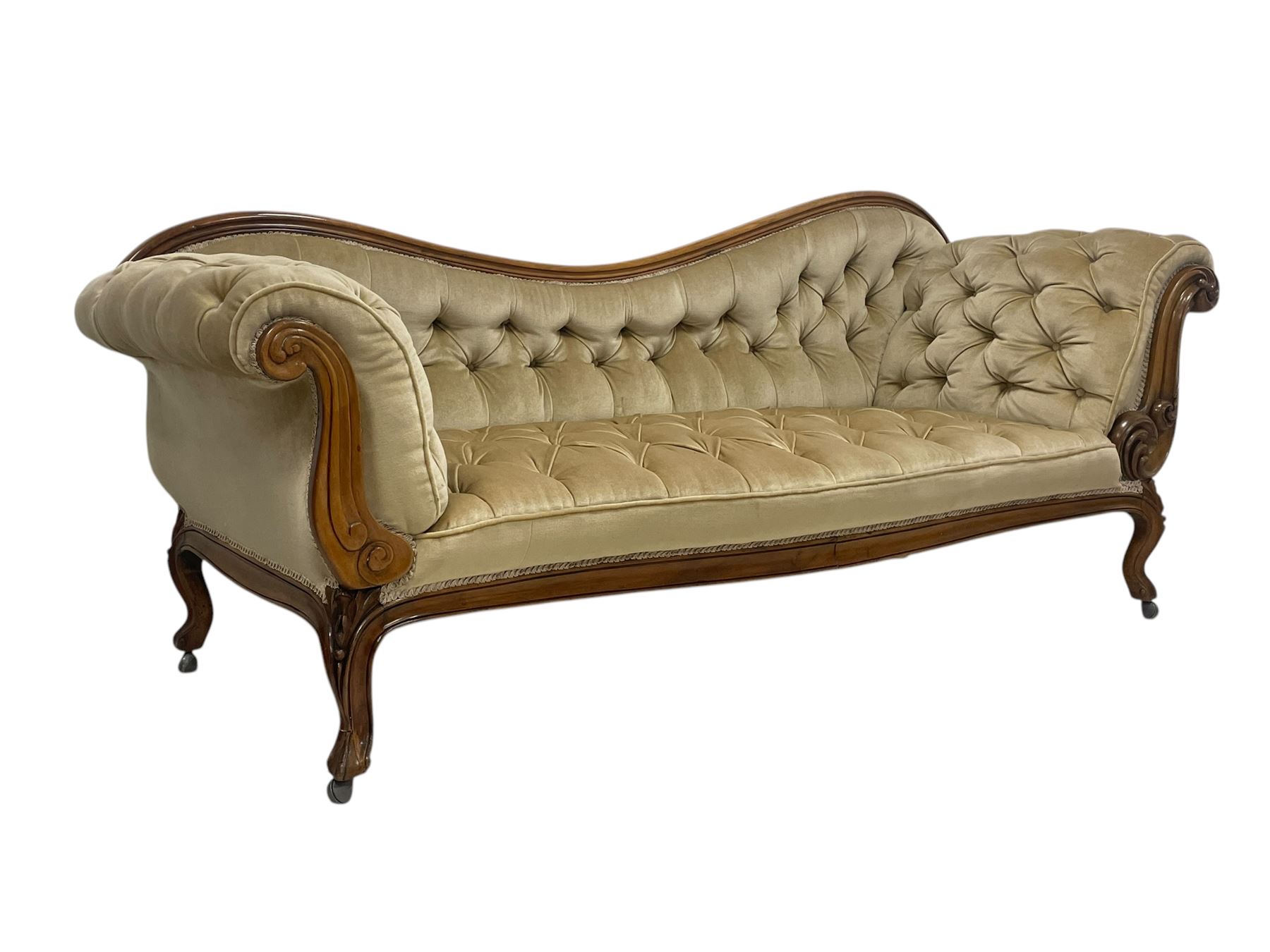 19th century walnut framed chaise longue, shaped back over scrolled arms decorated with moulded curling acanthus carvings, upholstered in deep buttoned champagne fabric, raised on cabriole supports with applied floral carved decoration, on castors