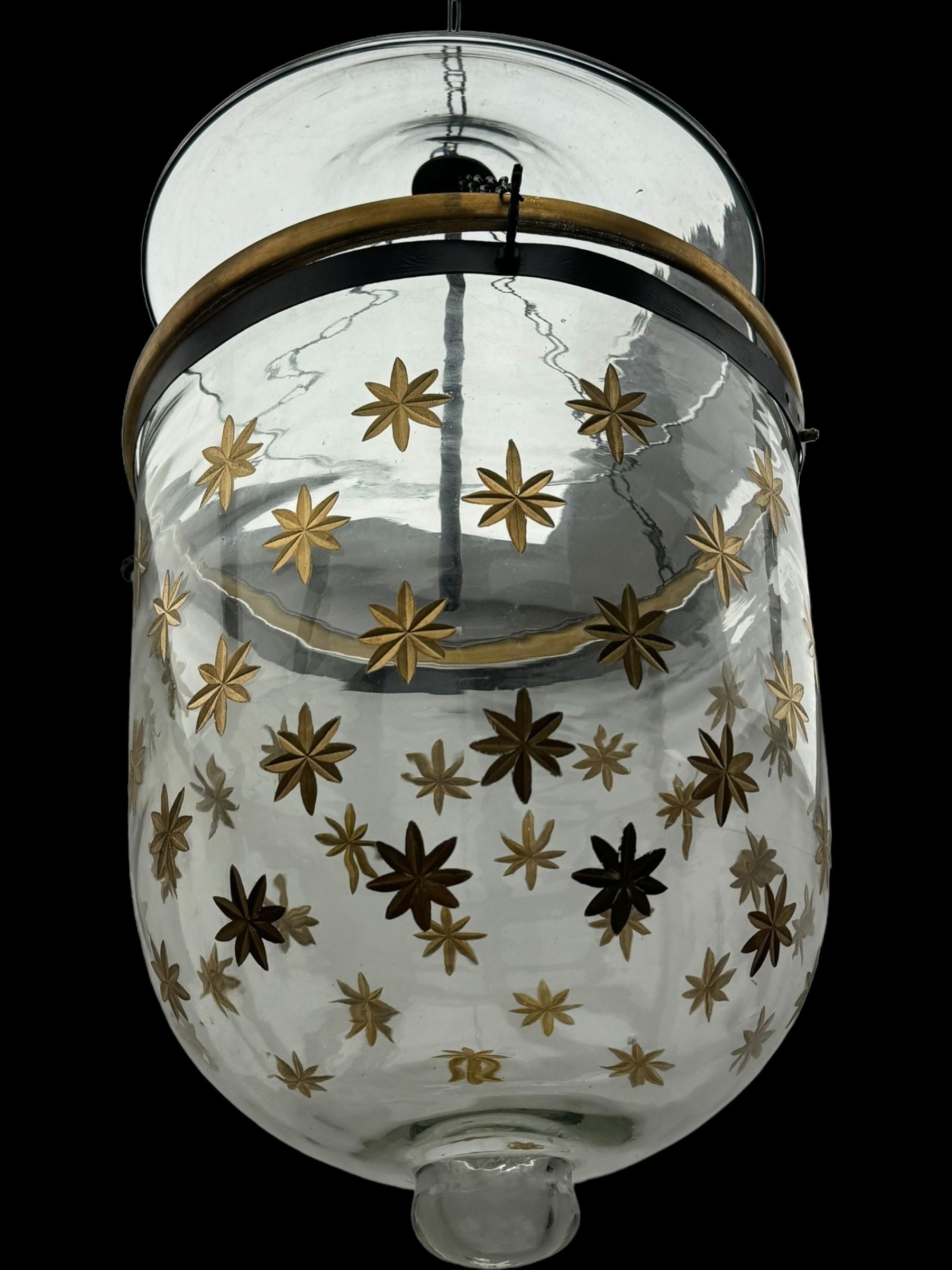 India Jane Interiors - pair of glass hanging lanterns, clear glass bell jars decorated with gold starburst patterns, each topped with a wide glass dish and suspended by three brass chains, the rim of each bell jar accentuated with a brass band, black metal hooks with a dragon head motif attach the chains to the rim