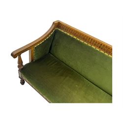 Late Victorian walnut framed sofa, rectangular backrest with carved detailing and central motif, upholstered in olive green fabric with brass studded trim and patterned front rail, scrolled fluted arms supported by turned uprights terminating in bun feet