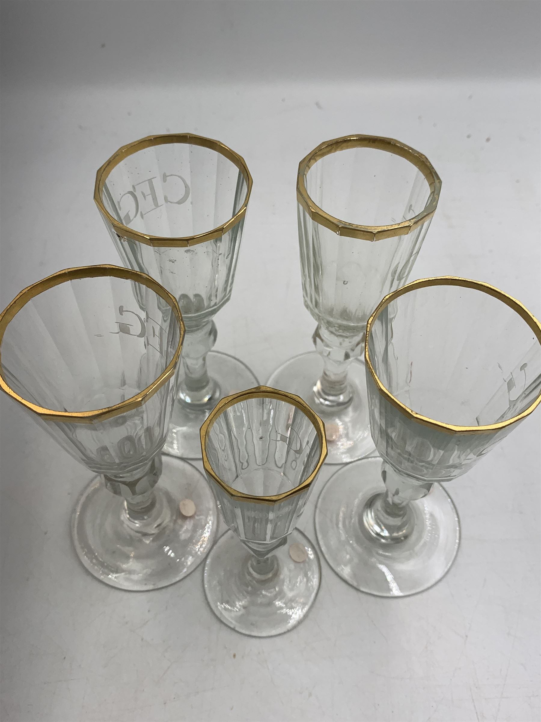 Set of four 19th century Baccarat liqueur/sherry glasses, circa 1820, with panelled bucket bowls and gilt rims, engraved CEG, to faceted knopped stems, together with another smaller example, H14cm and H12cm (5)