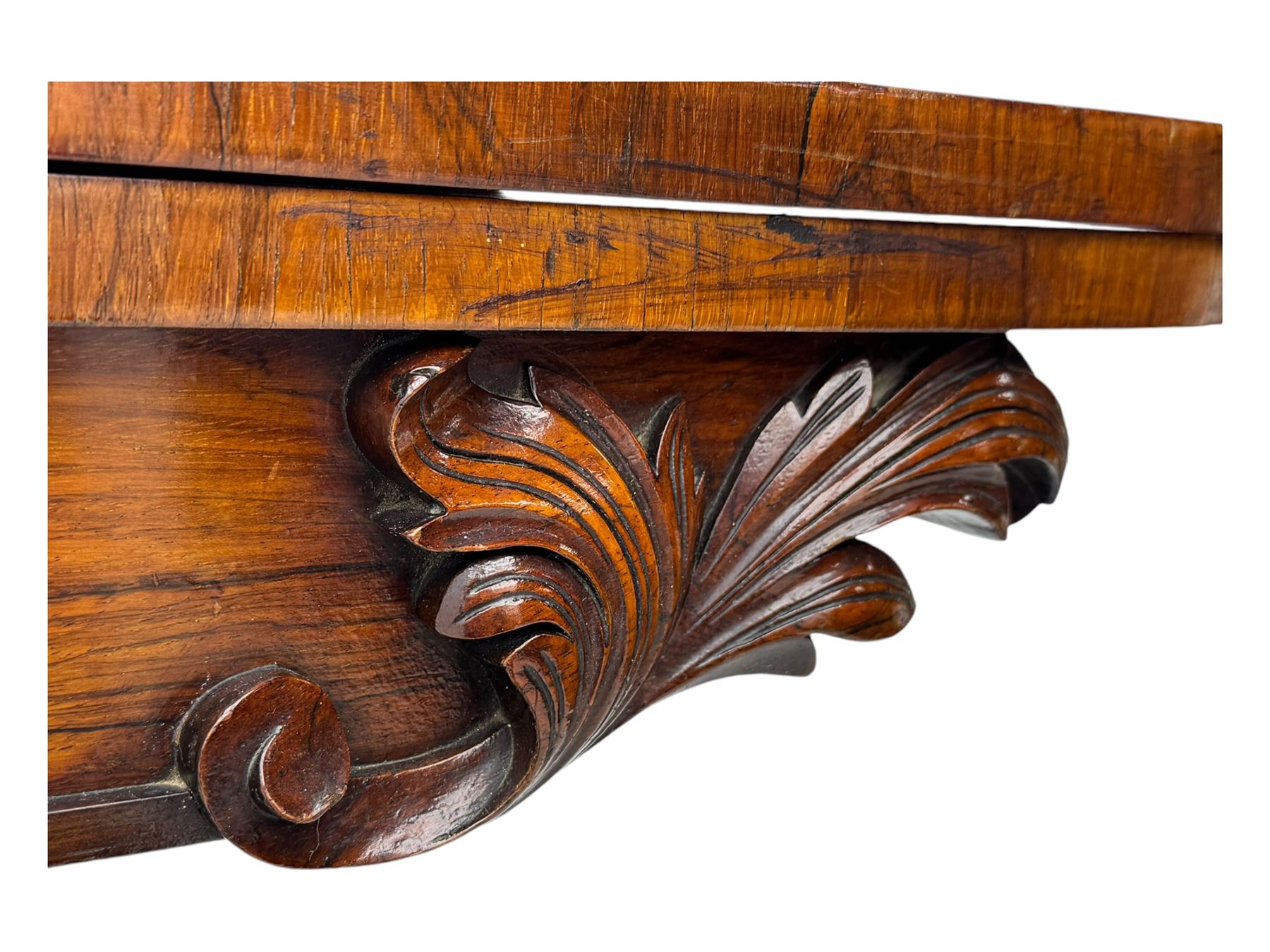 Early Victorian rosewood card table, rectangular foldover swivel top with rounded corners, red baize-lined surface, frieze adorned with carved foliate motifs, supported by a central octagonal waisted column on shaped quatrefoil base, terminating in scrolled feet with concealed metal castors