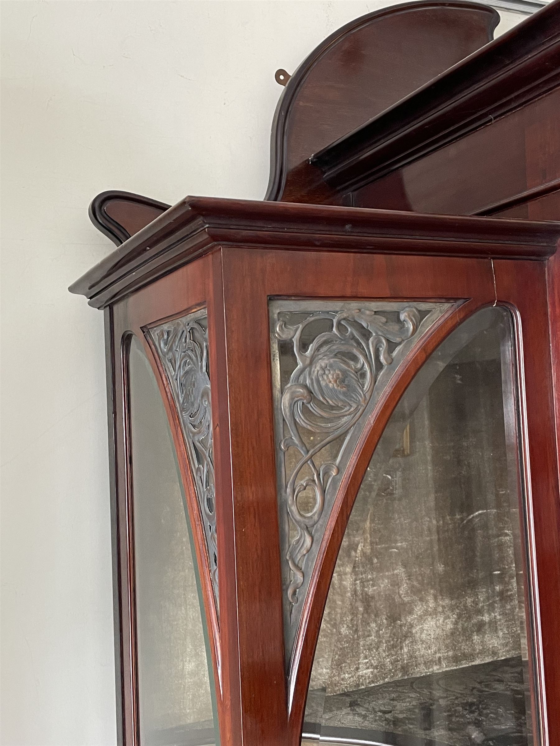 Art Nouveau period inlaid mahogany display cabinet, raised shaped and moulded pediment over projecting moulded cornices, the upper frieze inlaid with trailing branches and tulips, single astragal and bevel glazed door enclosed velvet lined interior fitted with shelves, flanked by curved glass panes decorated with pierced metal foliate spandrels, lower flanking shelves with mirror backs enclosed within shaped and pierced rails inlaid with flower heads, on tapering octagonal supports terminating to compressed pad feet, the lock stamped 'Salmon Bros, London' 