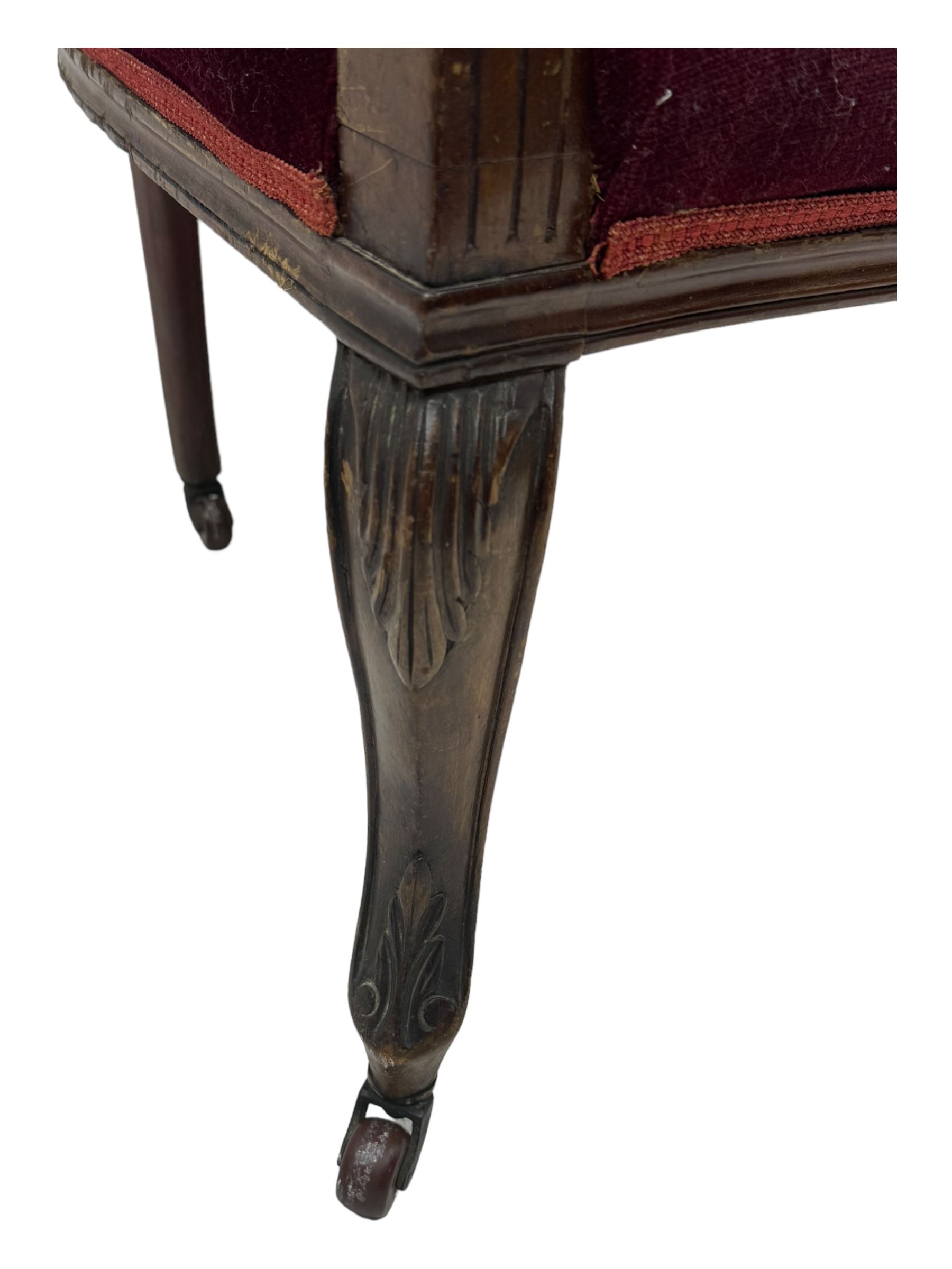 Late Victorian dark oak framed sofa, the backrests, seat and padded arms upholstered in deep red fabric, carved crest rail with scroll and foliate motifs supported by carved uprights, on cabriole supports with leaf carvings terminating in castors