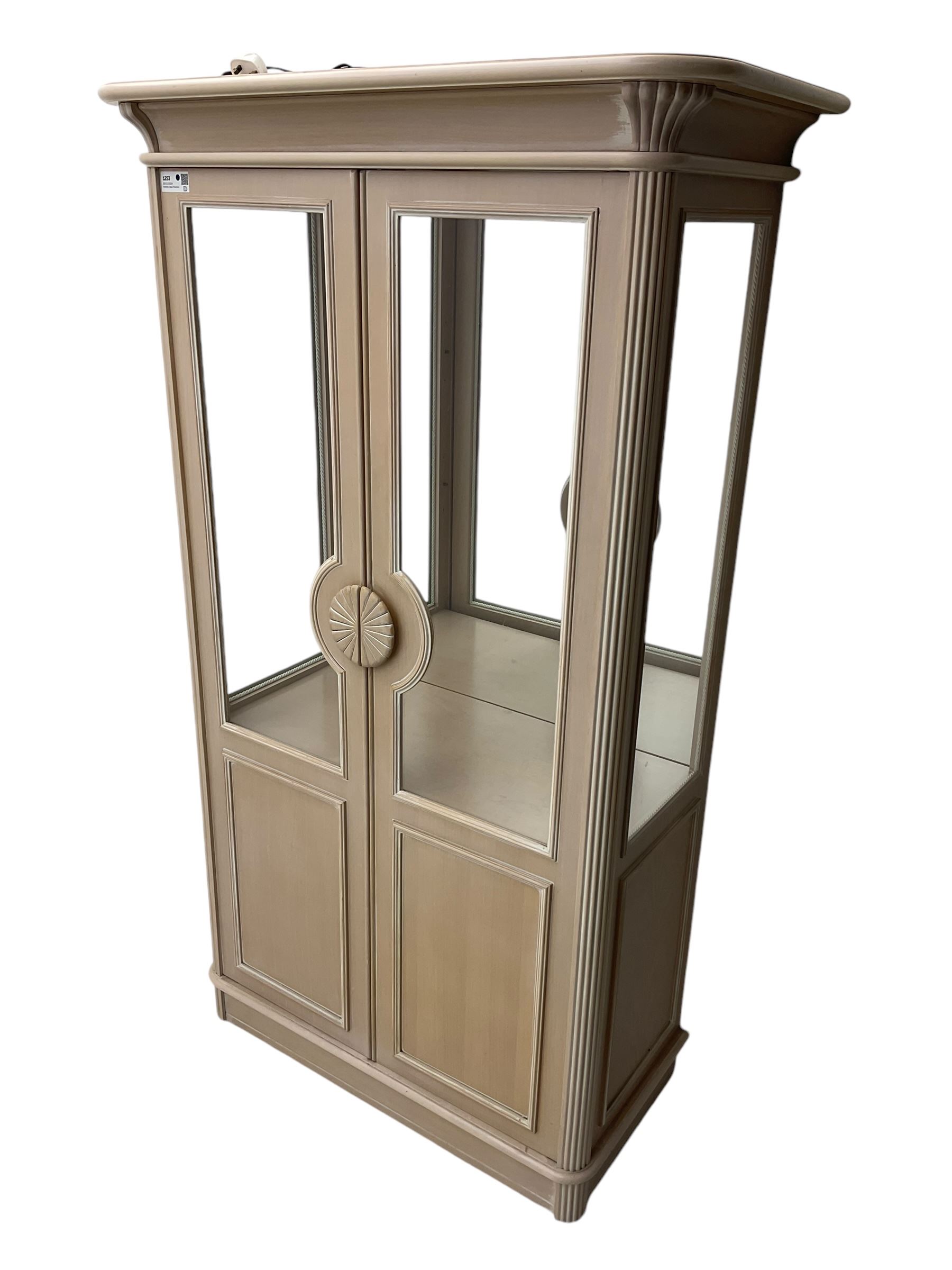 Contemporary display cabinet, moulded cornice above glazed panelled doors with central carved sunburst handles, mirrored back interior with lighting, lower enclosed storage compartment, raised on plinth base