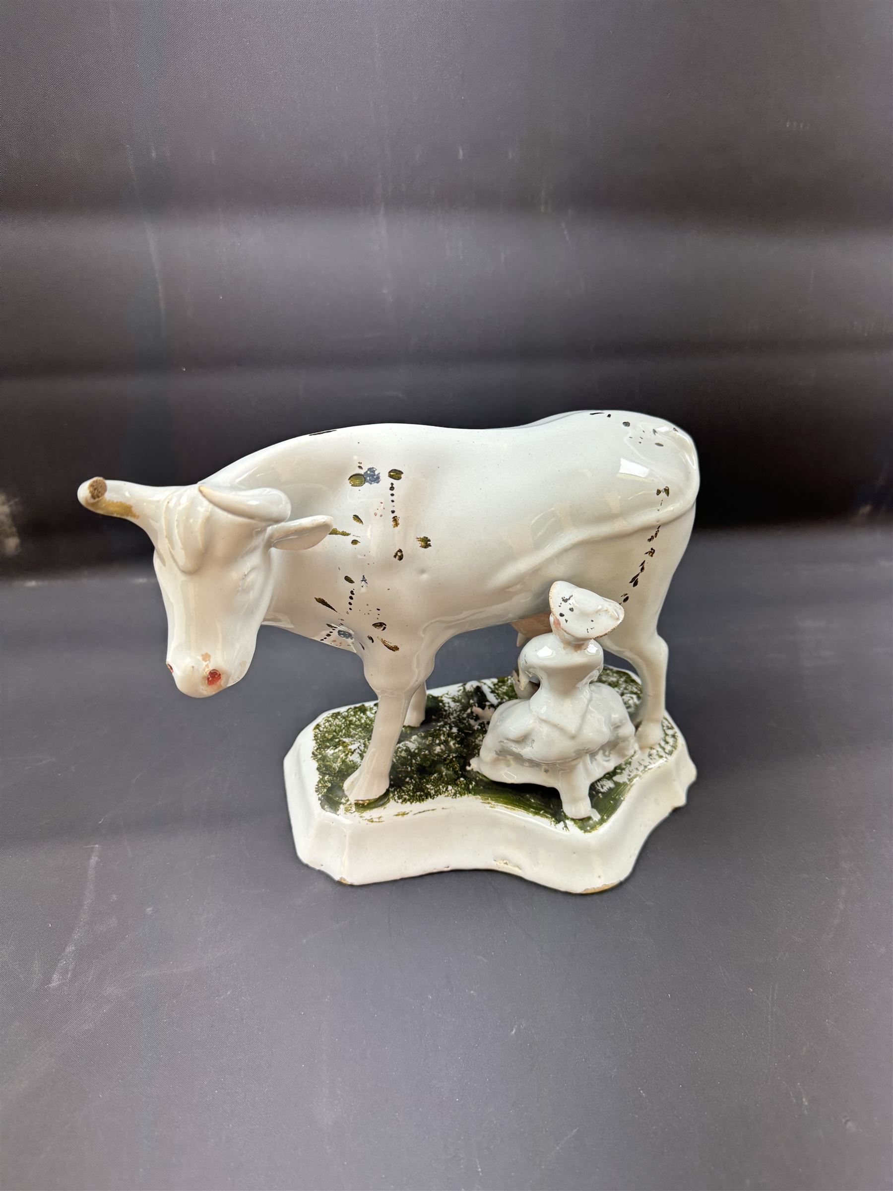 19th century Delft figure group depicting a milkmaid milking a cow, H17.7cm