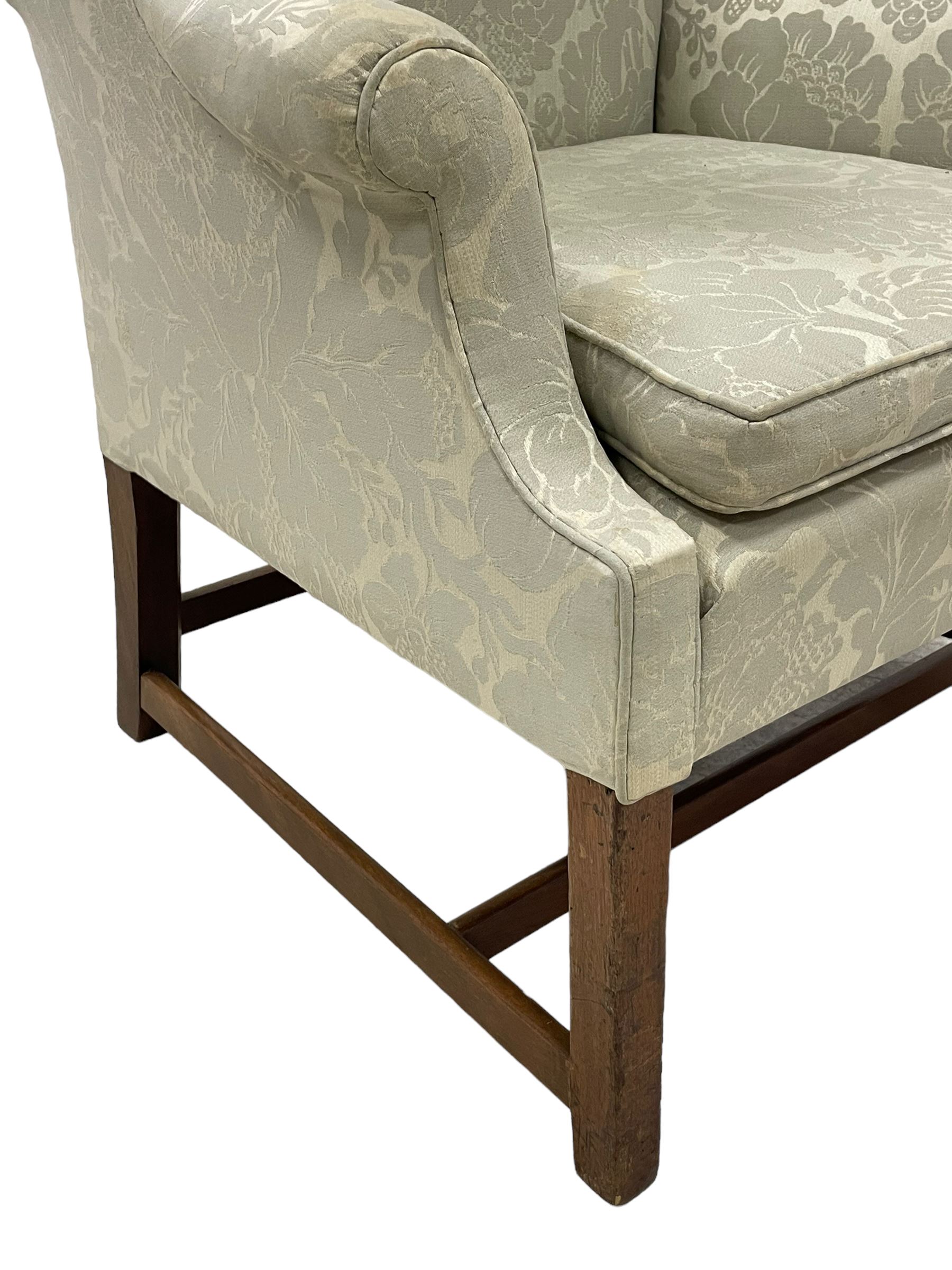 Georgian mahogany framed wingback armchair, upholstered in floral pattern silk damask fabric, wide seat enclosed by rolled arms, on chamfered square supports united by plain stretchers 