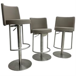 Three contemporary polished metal adjustable Monza bar stools, with taupe faux leather upholstered seats, supported by a brushed stainless steel pedestal base with integrated footrests