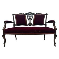 Late Victorian dark oak framed sofa, the backrests, seat and padded arms upholstered in deep red fabric, carved crest rail with scroll and foliate motifs supported by carved uprights, on cabriole supports with leaf carvings terminating in castors