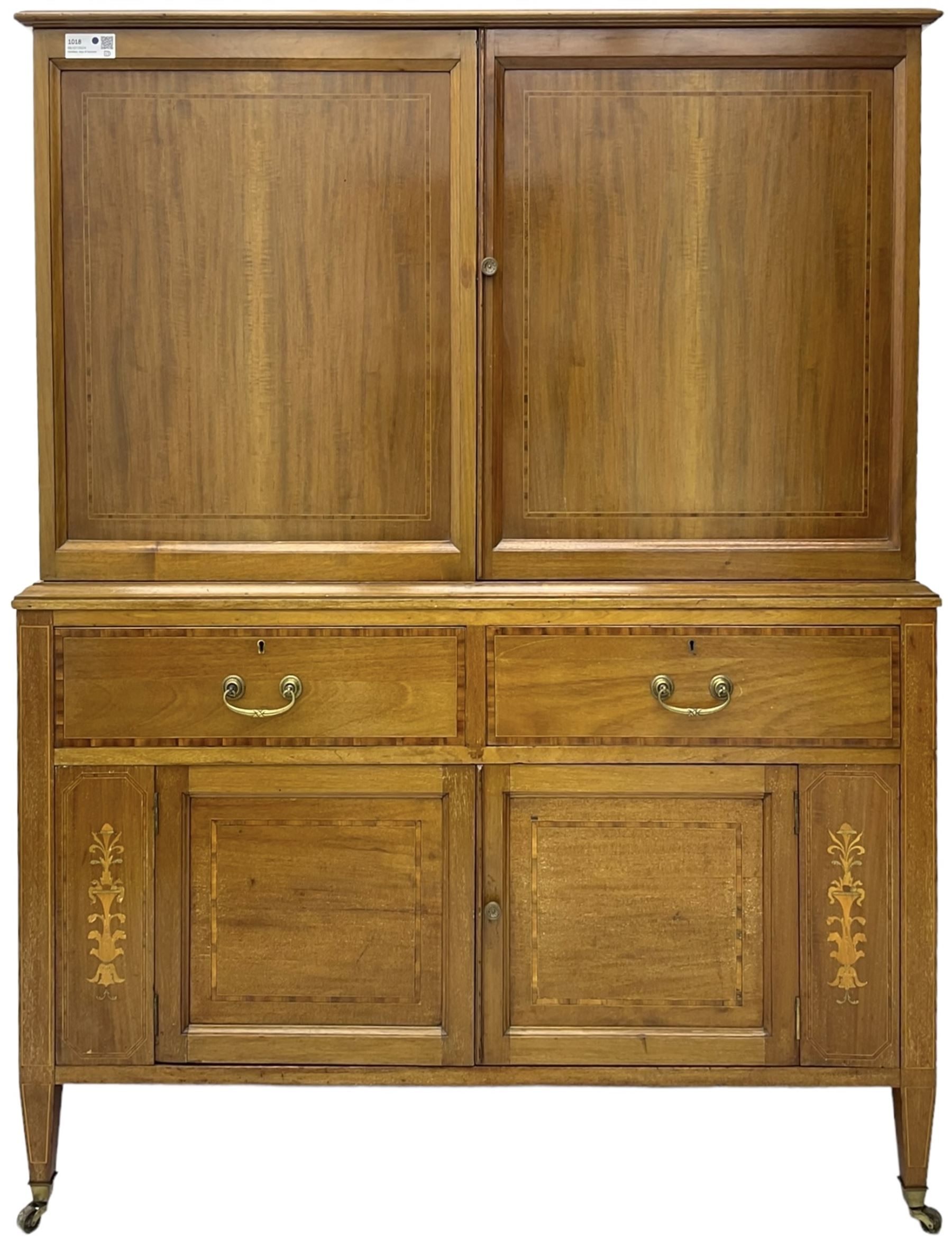 Early 20th century inlaid mahogany cabinet, two-door upper section revealing interior shelving and two large pull-out drawers, the lower section comprises two wide drawers flanked by inlaid floral motif panels above a double-door cupboard, supported by tapering legs with brass castors