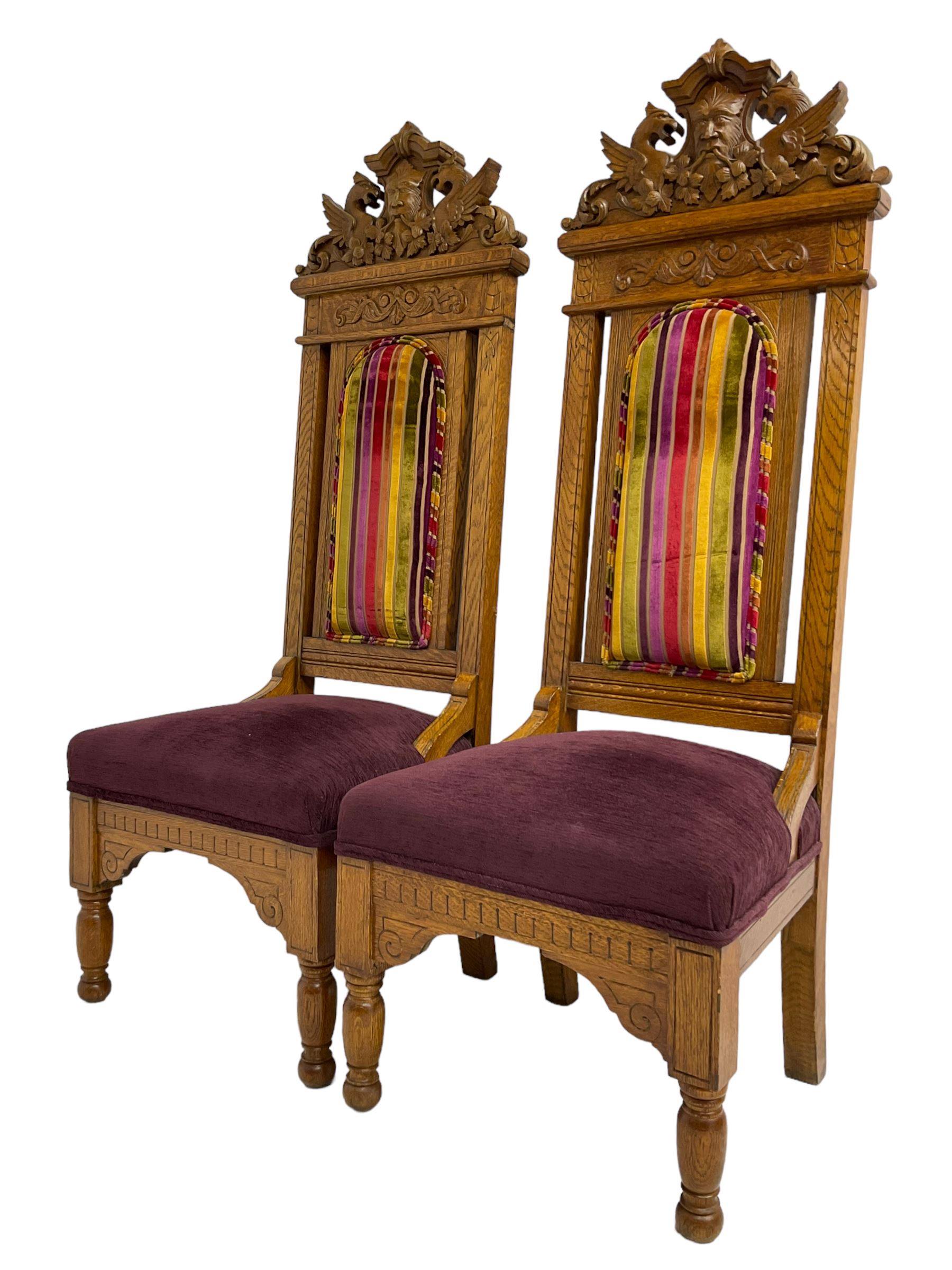 Set of six 20th century Carolean design oak high back chairs, the pediment carved with dragons and central Green Man mask with trailing foliage, the backs upholstered in striped fabric, on turned front supports